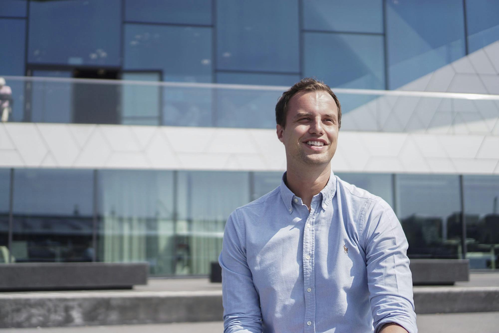 NextGenner Jesse Groenewegen glimlacht voor modern kantoor met glazen wanden.