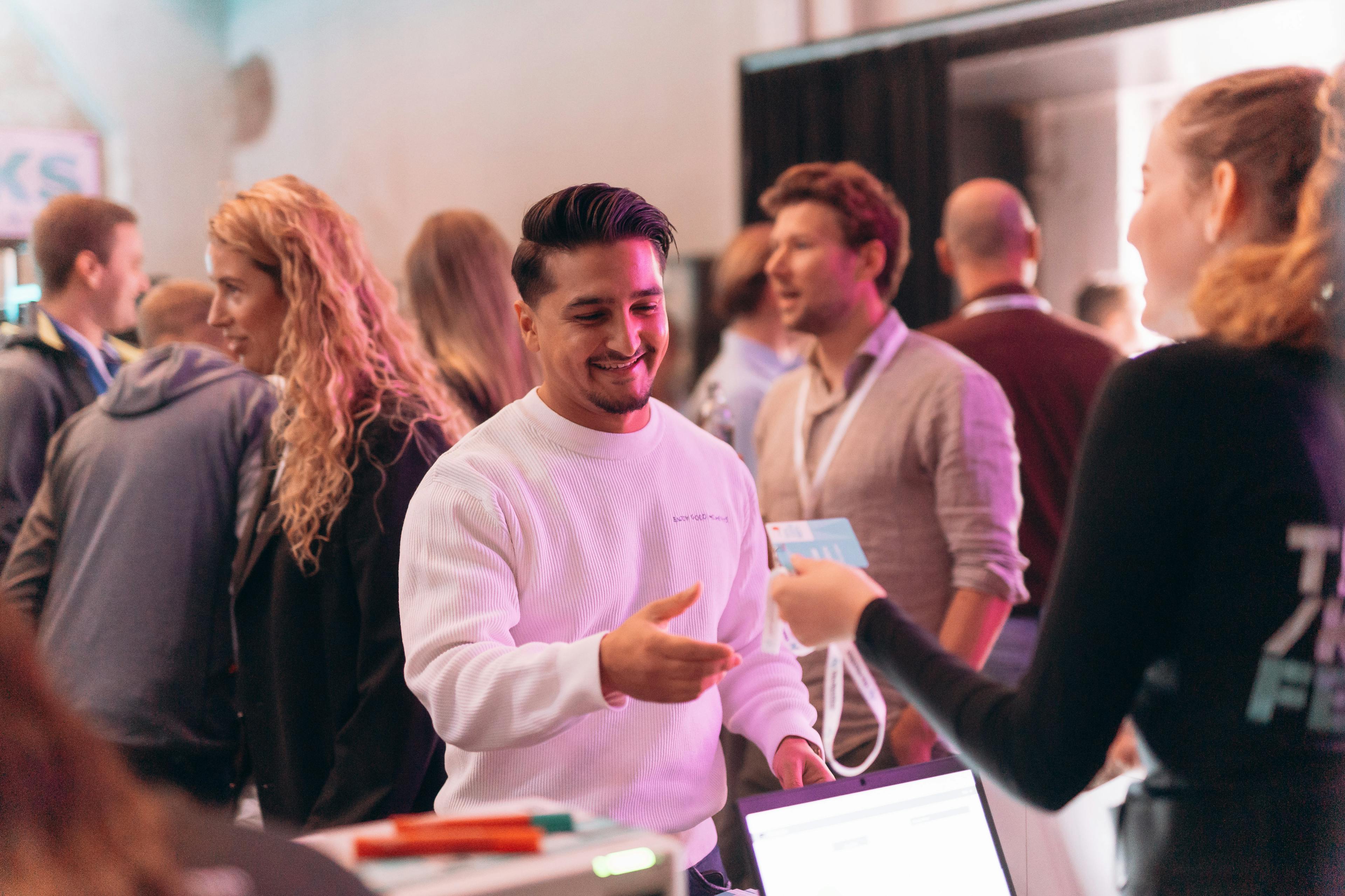 A man accepts a pass to an event from a woman wearing a Tech Know Fest t-shirt.