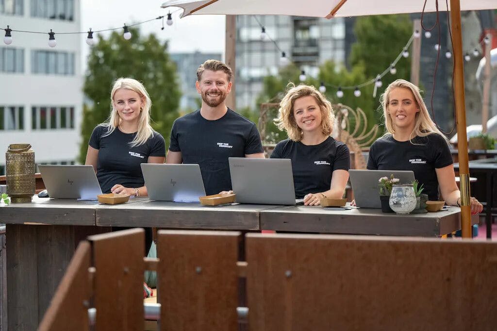 Vier NextGen medewerkers staan klaar om IT specialisten te verwelkomen tijdens een event.