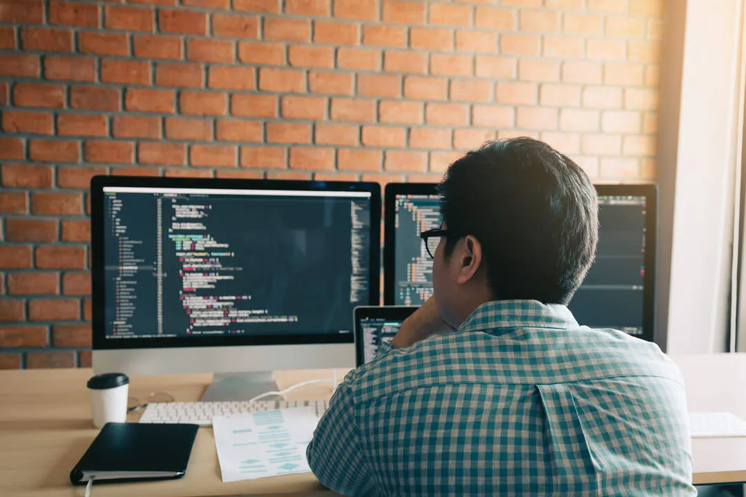 Java developer zit achter zijn bureau met twee schermen.