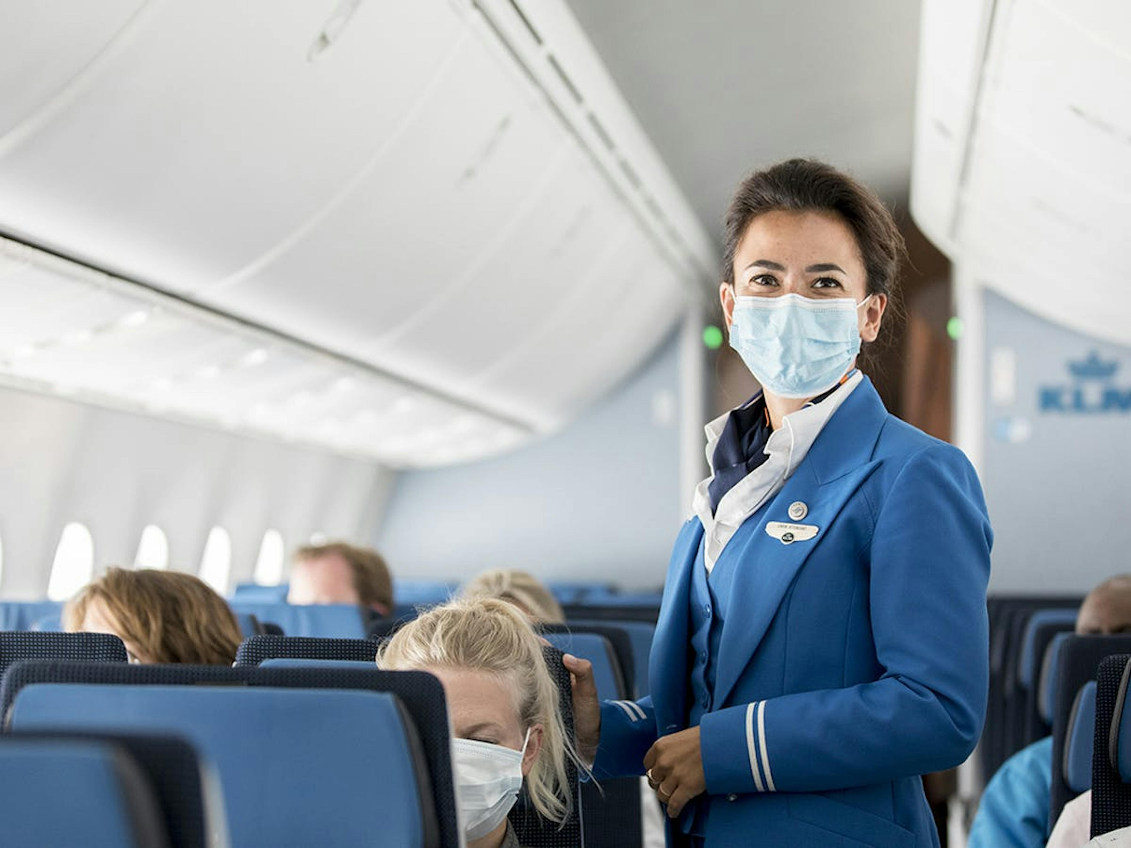 Een stewardess met mondkapje staat in het gangpad van een vliegveld.