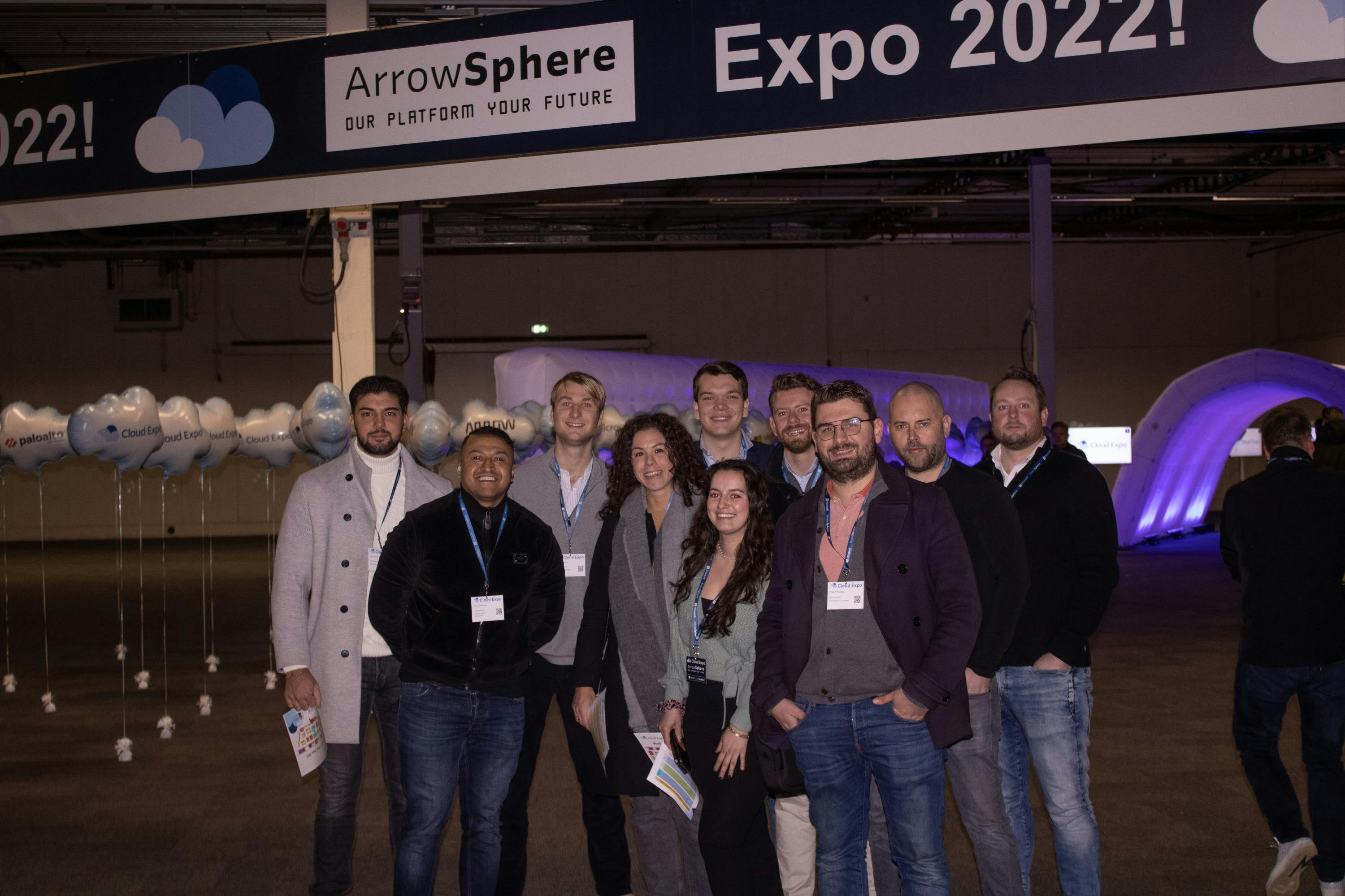 Een groep medwerkers van The.NextGen poseert voor de camera bij de ingang van de Cloud Expo 2022.