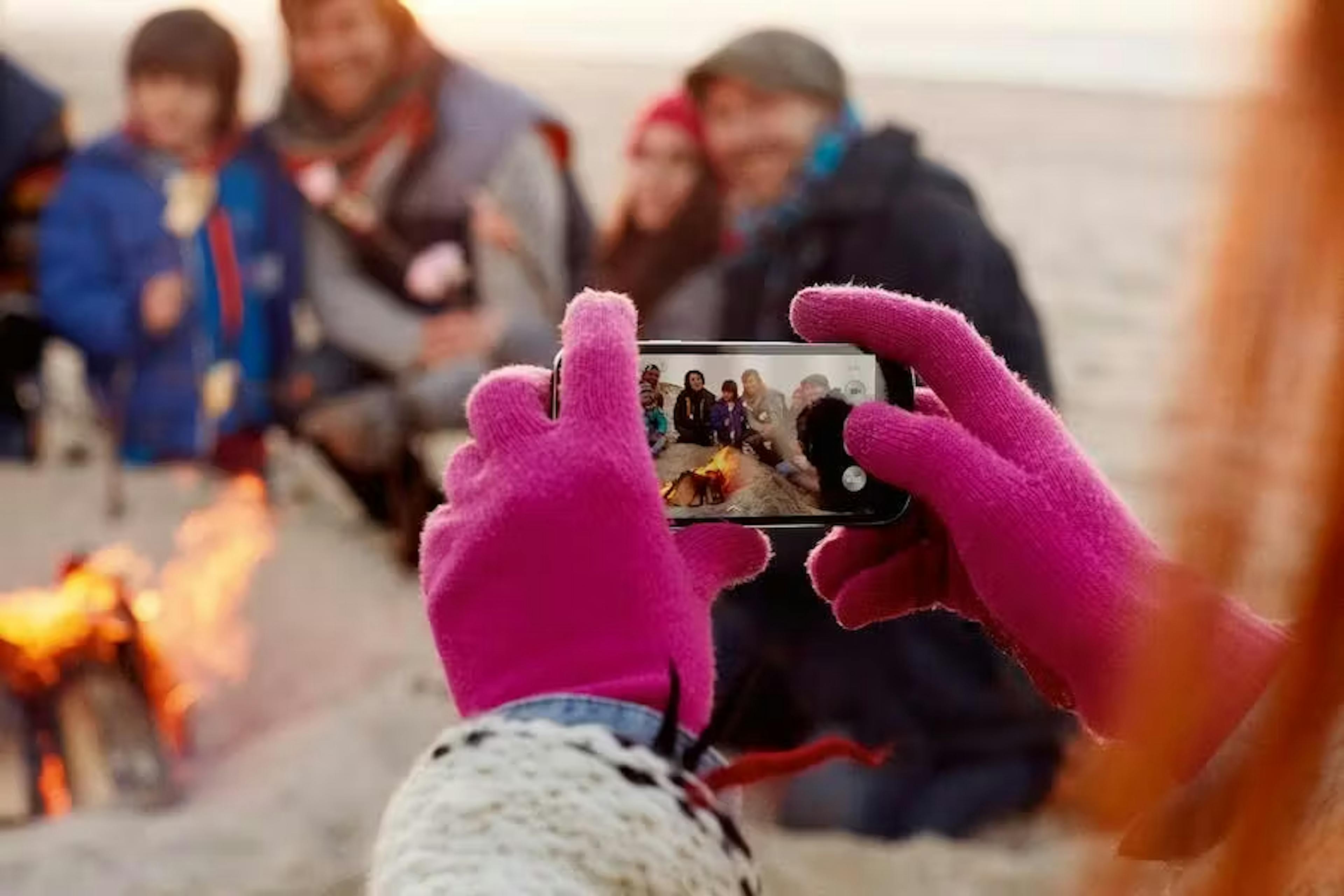 Roze handschoenen die een telefoon vasthoudt om gezellige foto te maken op het strand.