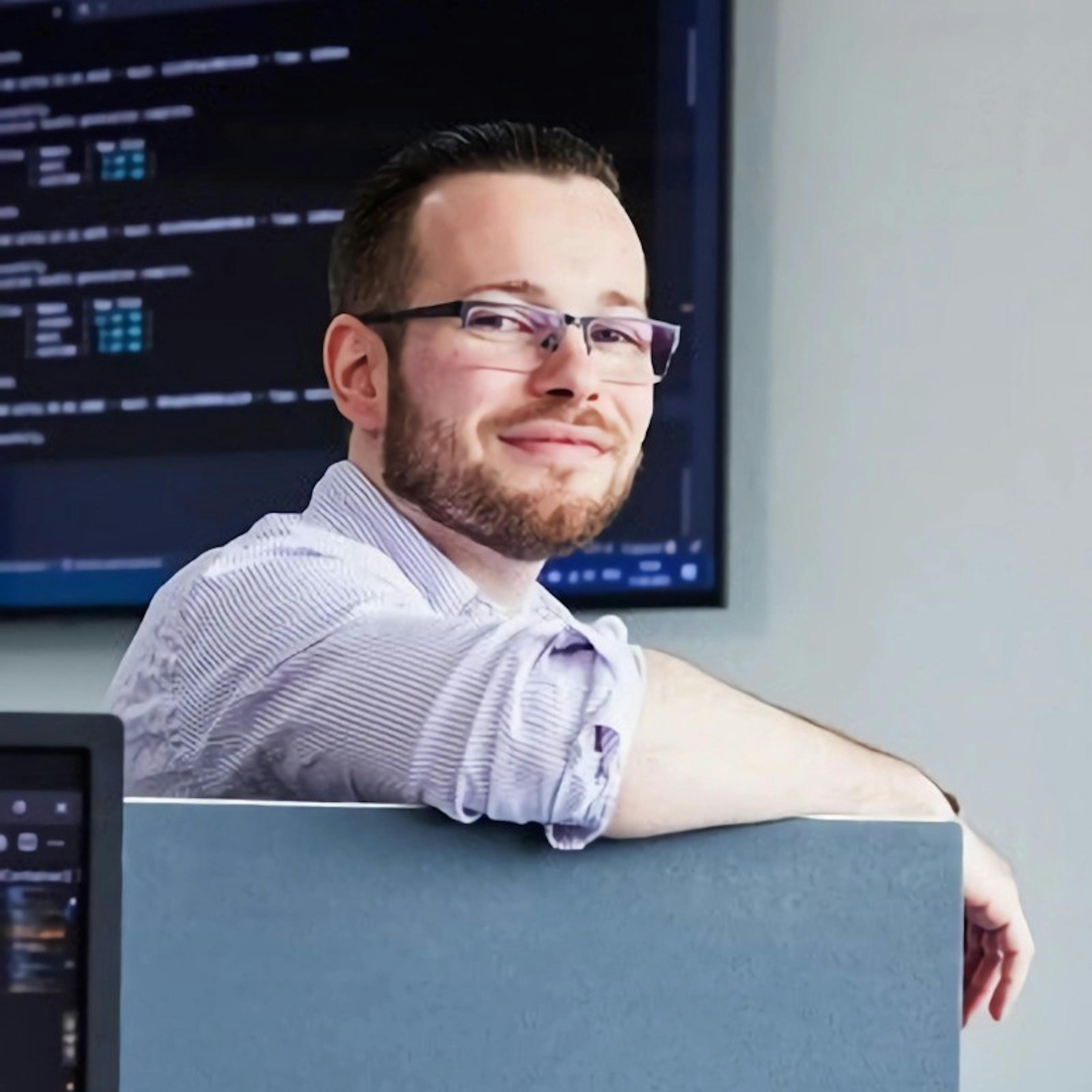 NextGenner Martin sits facing the camera in front of a screen displaying code. 