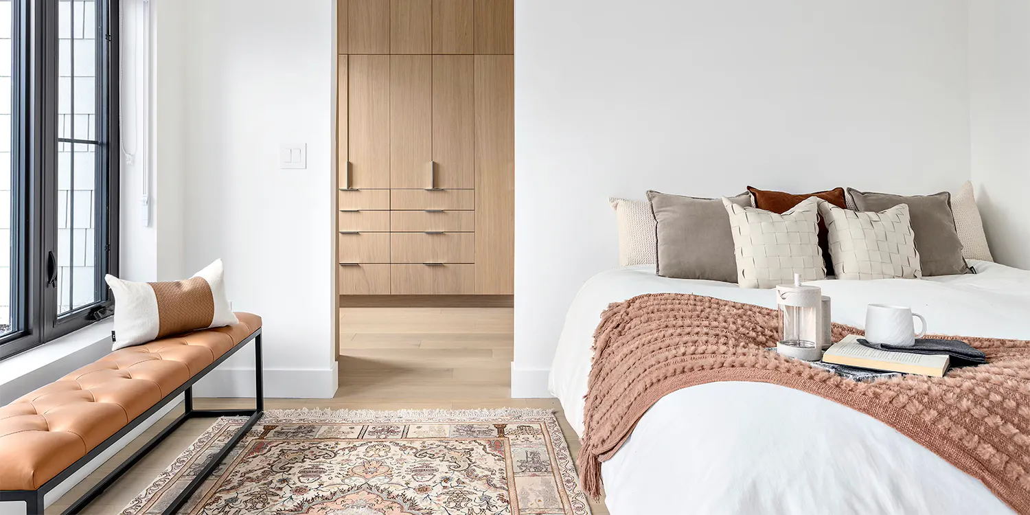 Modern bedroom with white bedding, wood cabinetry, and a window bench.