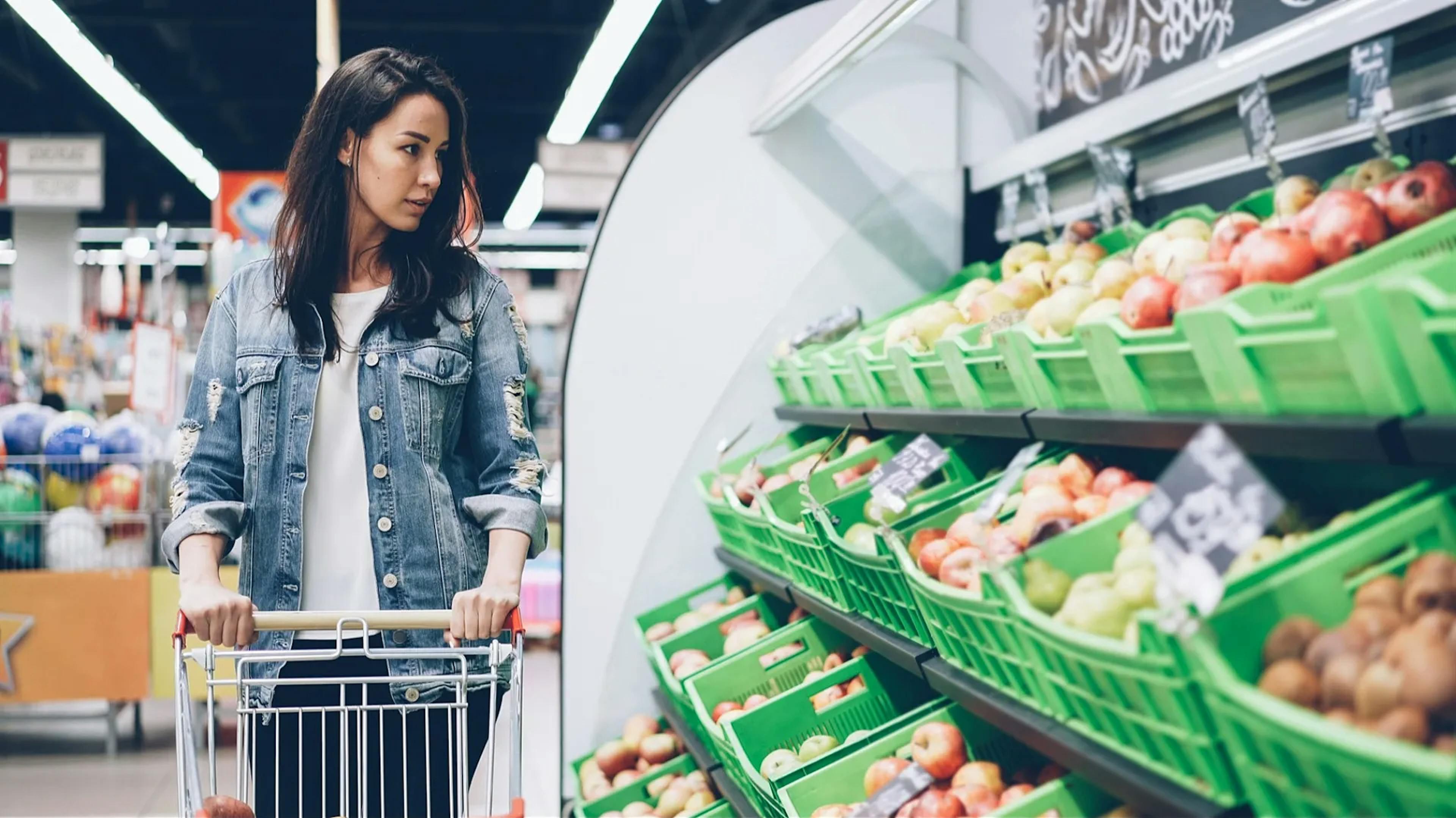 Woman with shopping cart in front of vegetable aisle