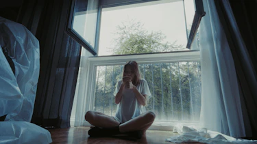 Suffocating visual cut from clip. A seated woman smoking from of a window