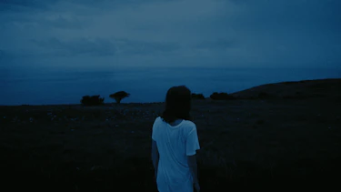Suffocating visual cut from clip. A standing woman in a field.