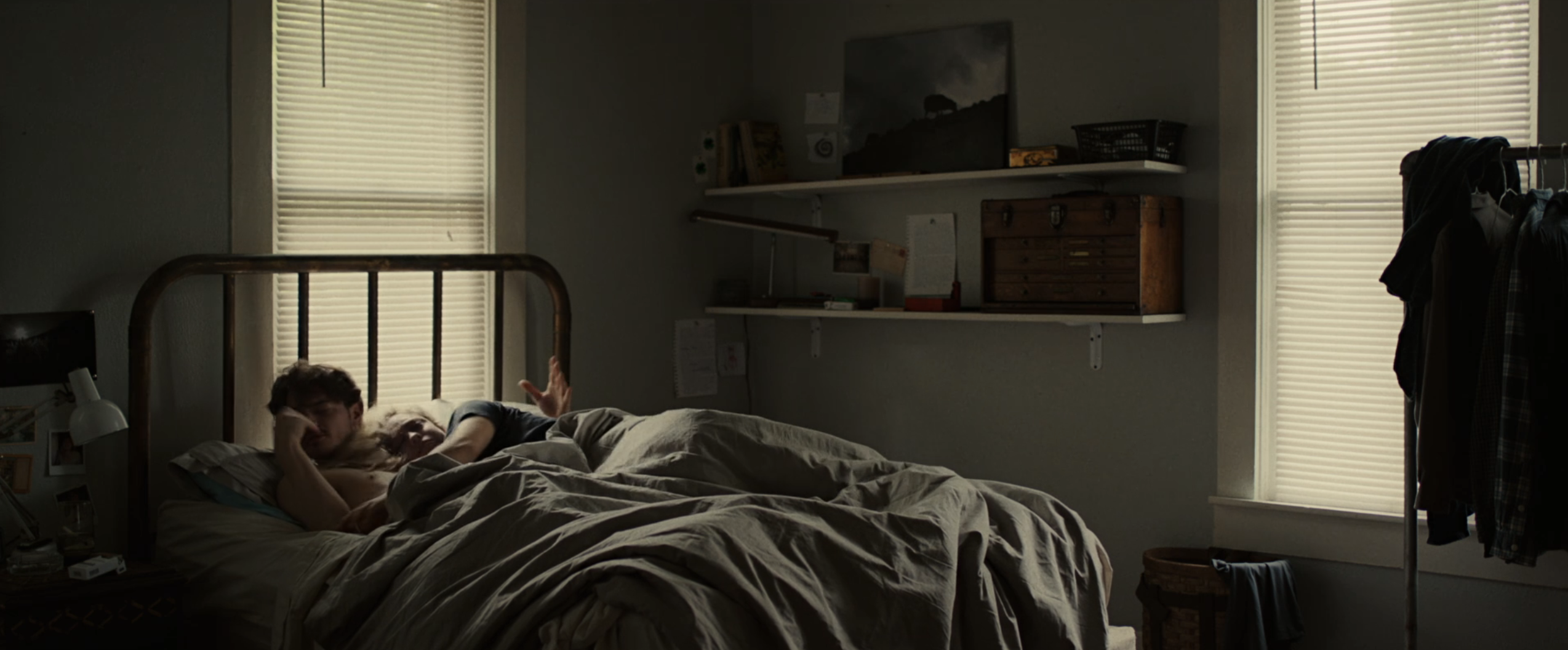Two people lay on a bed in a dark room with the shades down
