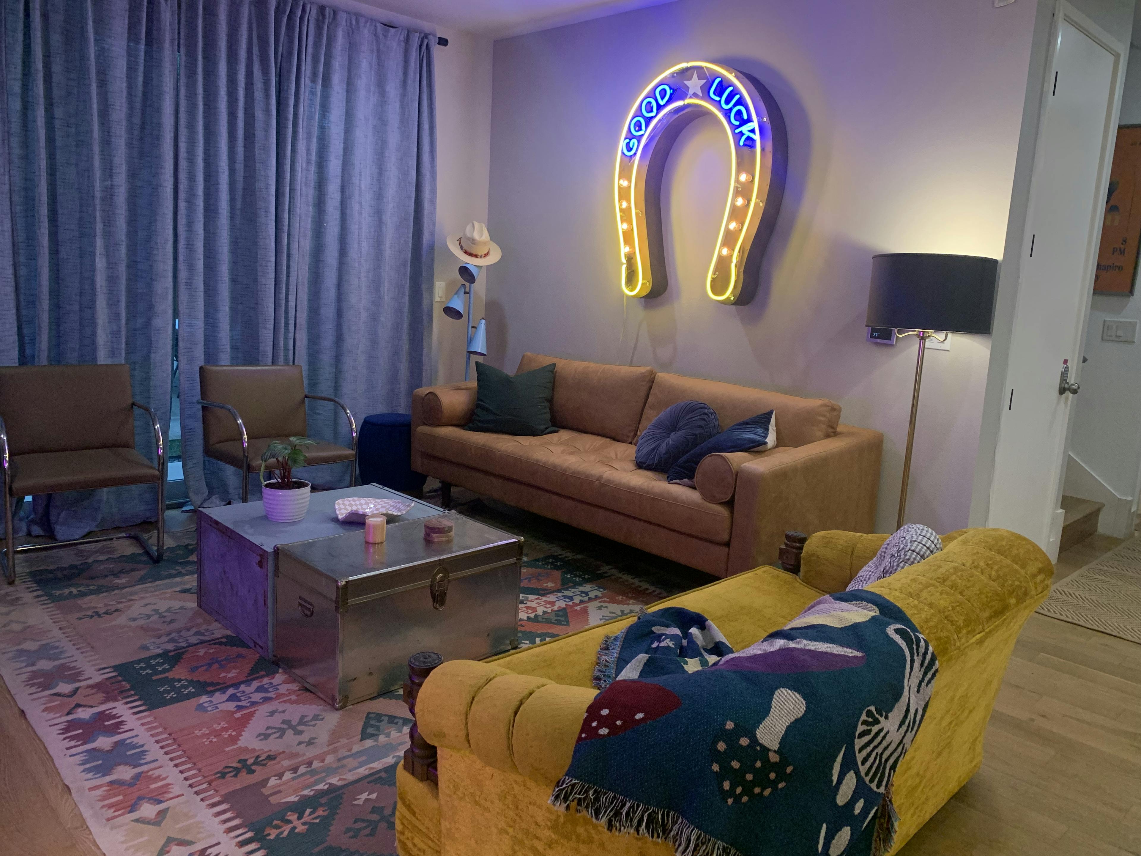 Two couches and chairs sit around a coffee table with a neon horseshoe with the text "Good luck" on the wall