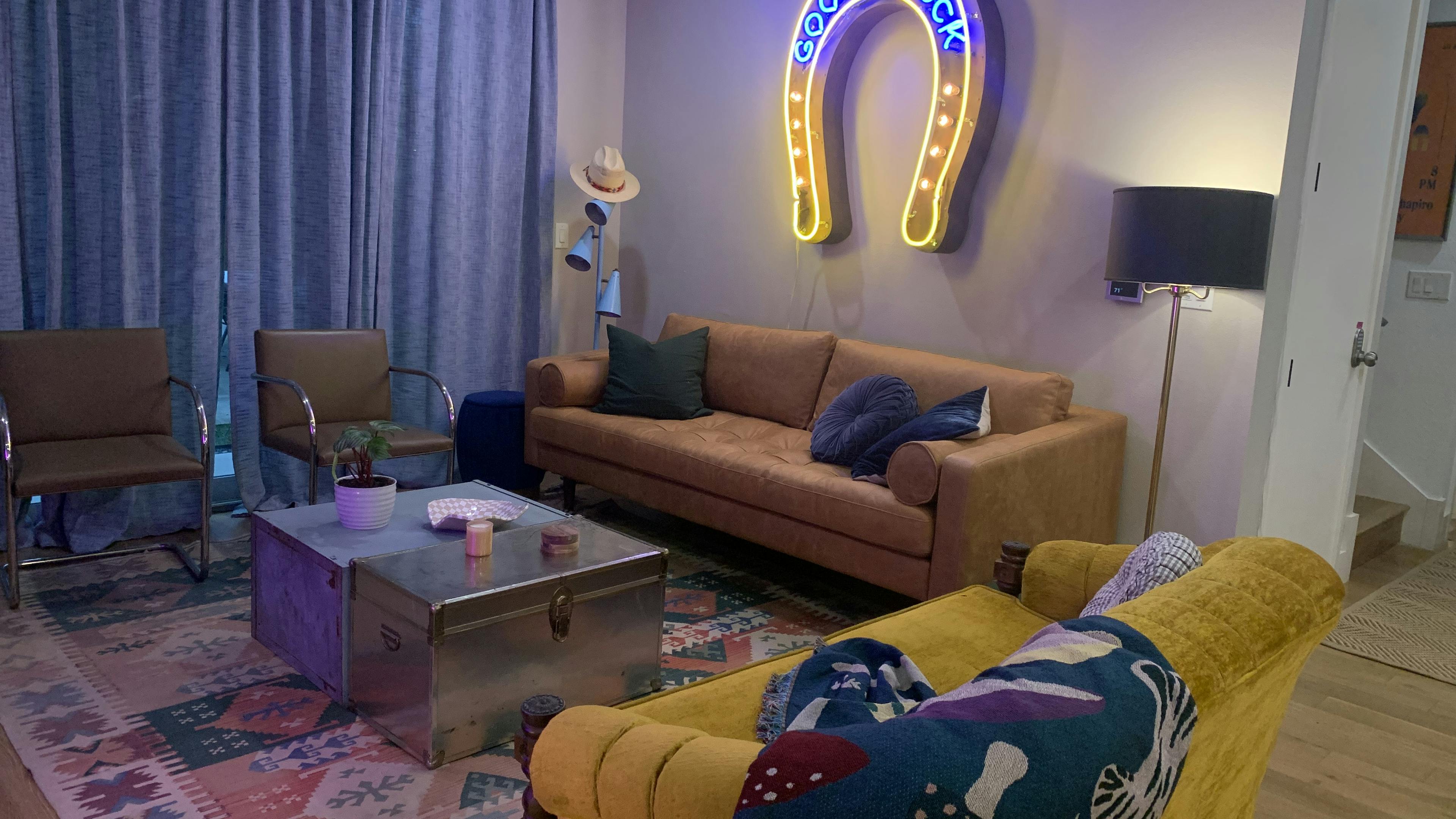 Two couches and chairs sit around a coffee table with a neon horseshoe with the text "Good luck" on the wall