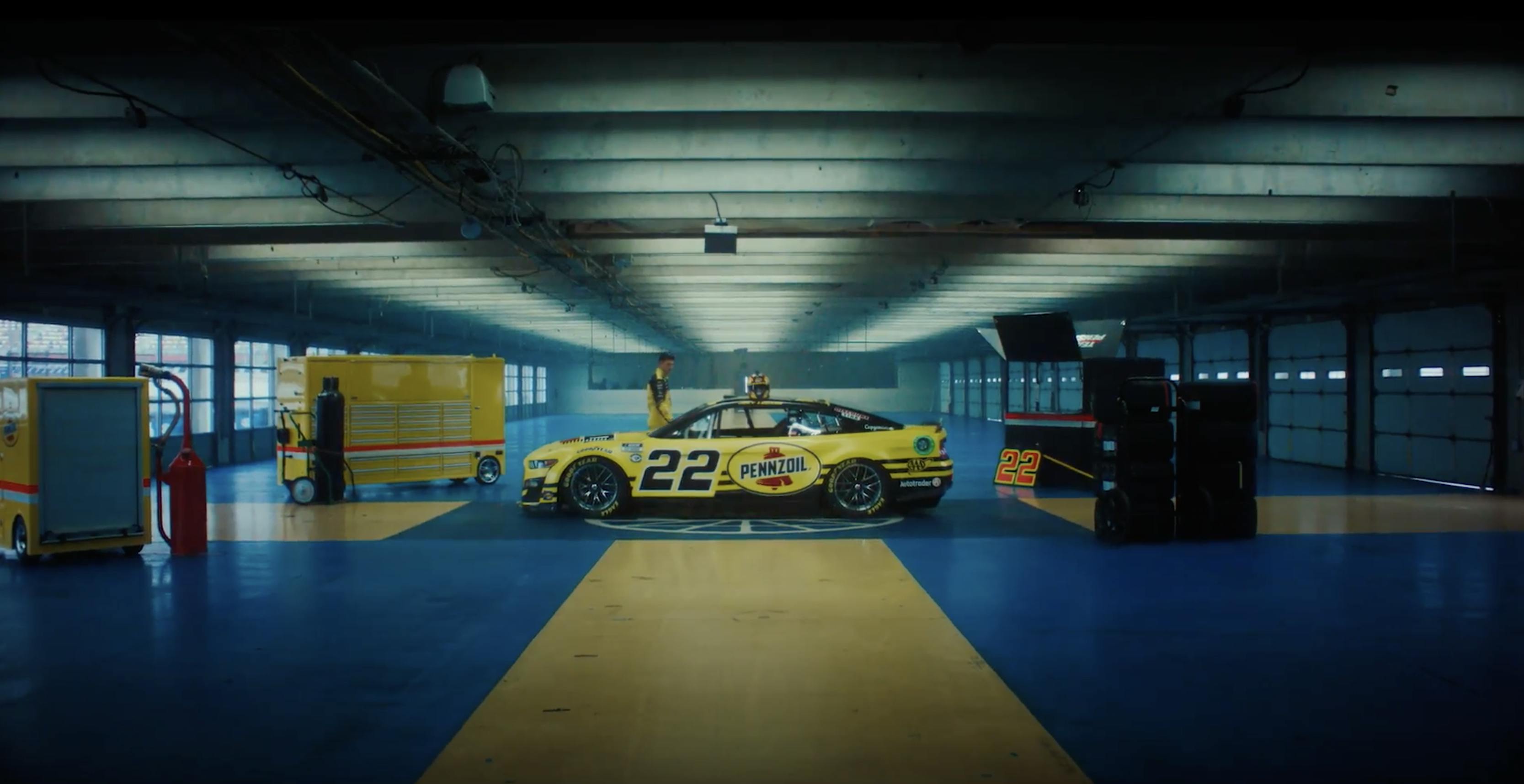 A yellow racecar with the Pennzoil logo sits in a large blue and yellow room