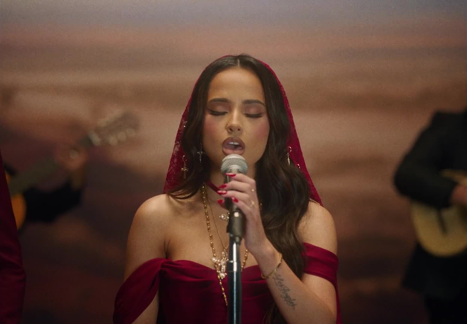 A woman in a red dress and veil sings into a microphone