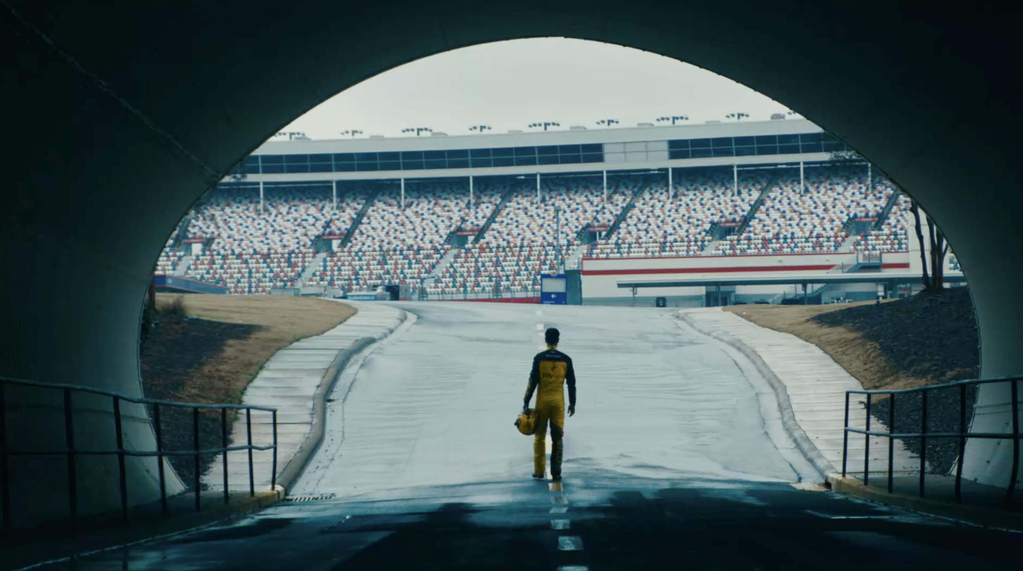 A racecar driver enters the race track, framed by a large tunnel