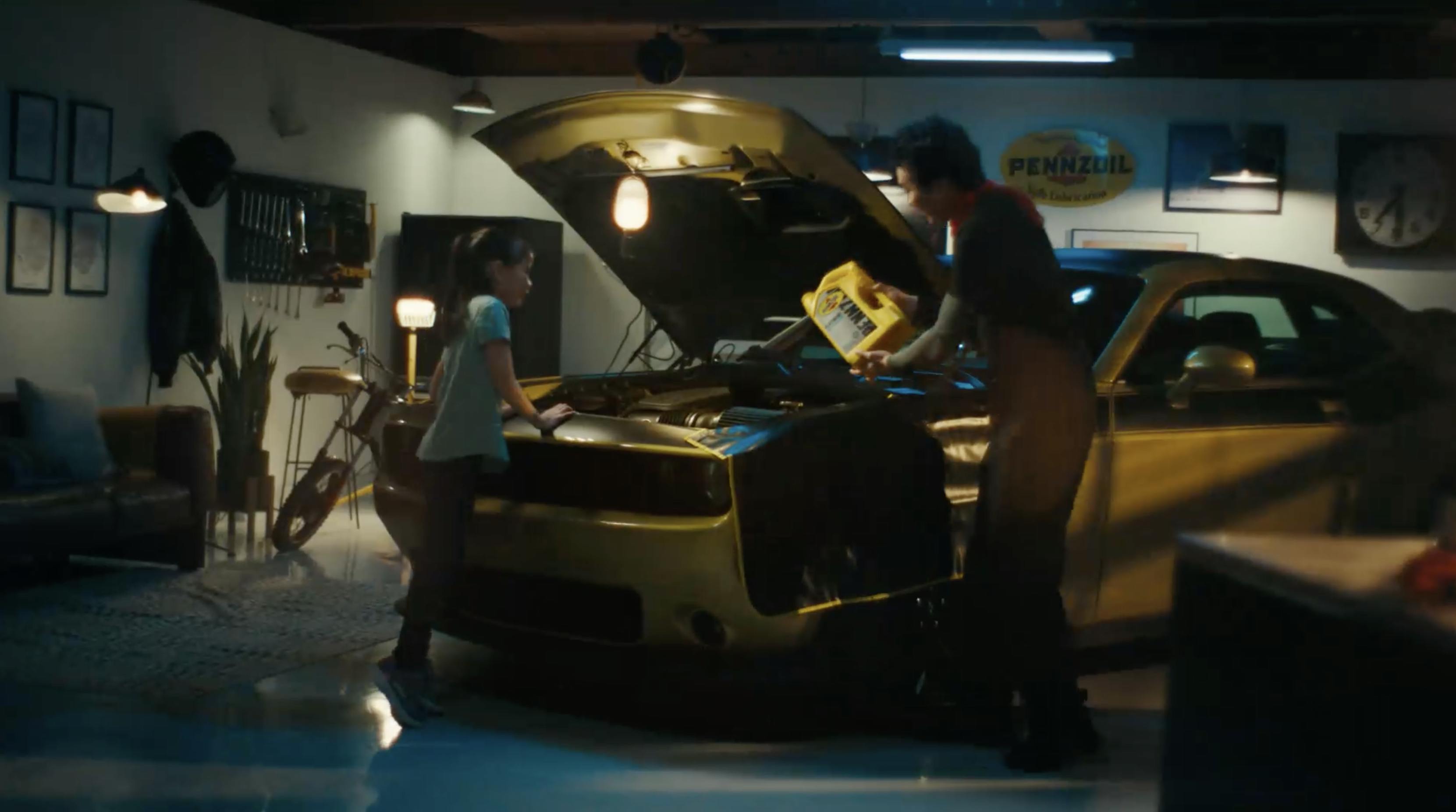 A man and a young girl pour Pennzoil into a yellow car
