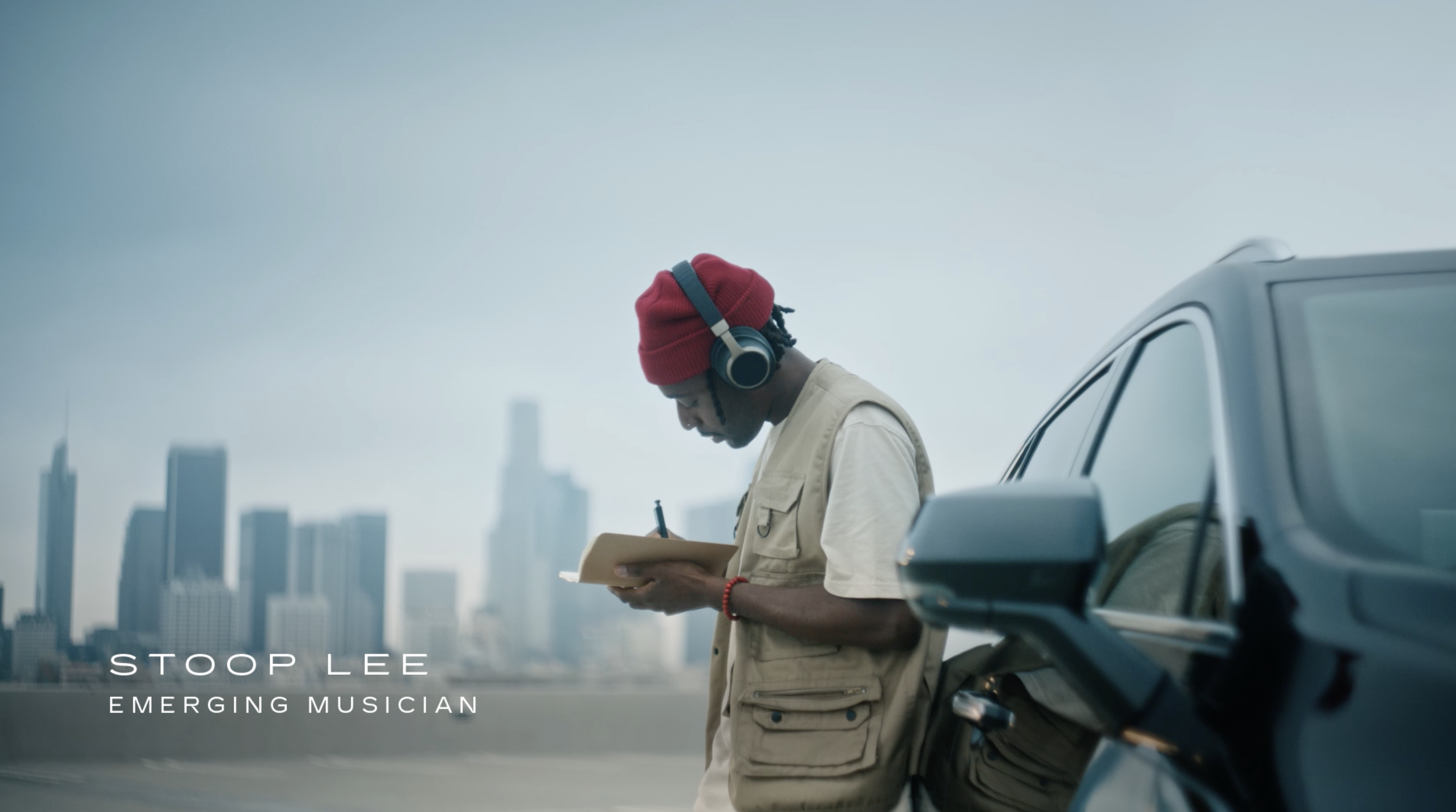 Musician writing in a notebook and leaning against a car