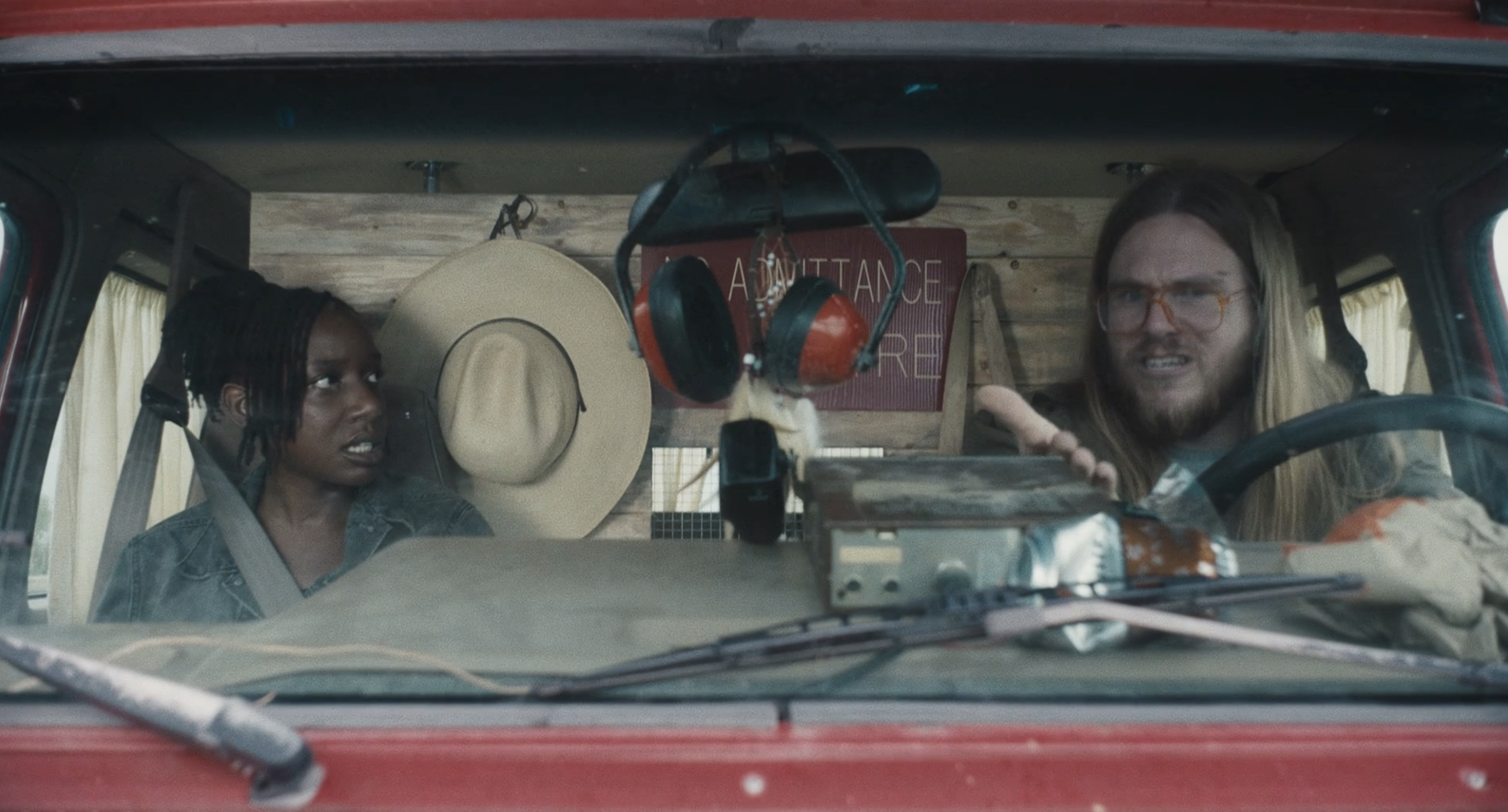 Two people sit in a red van arguing