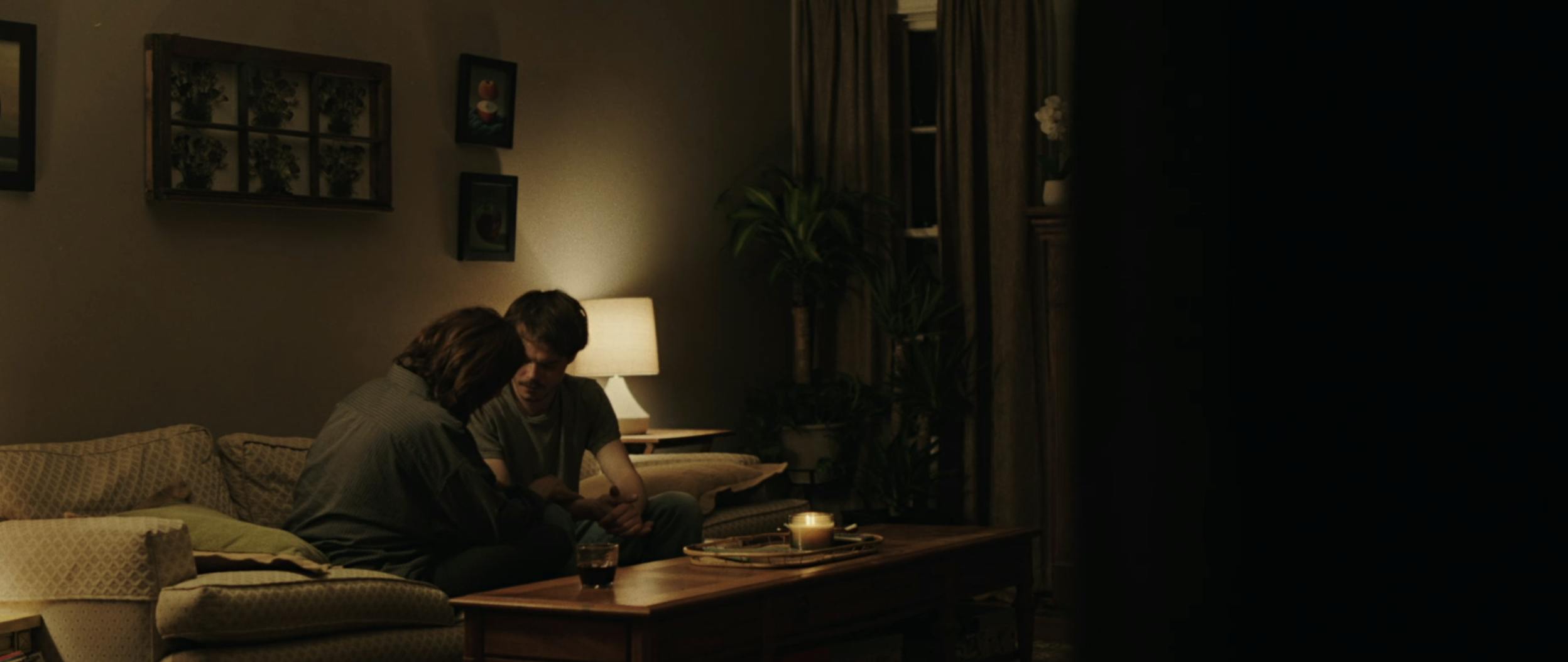 Two people sit on a couch in a dimly lit room