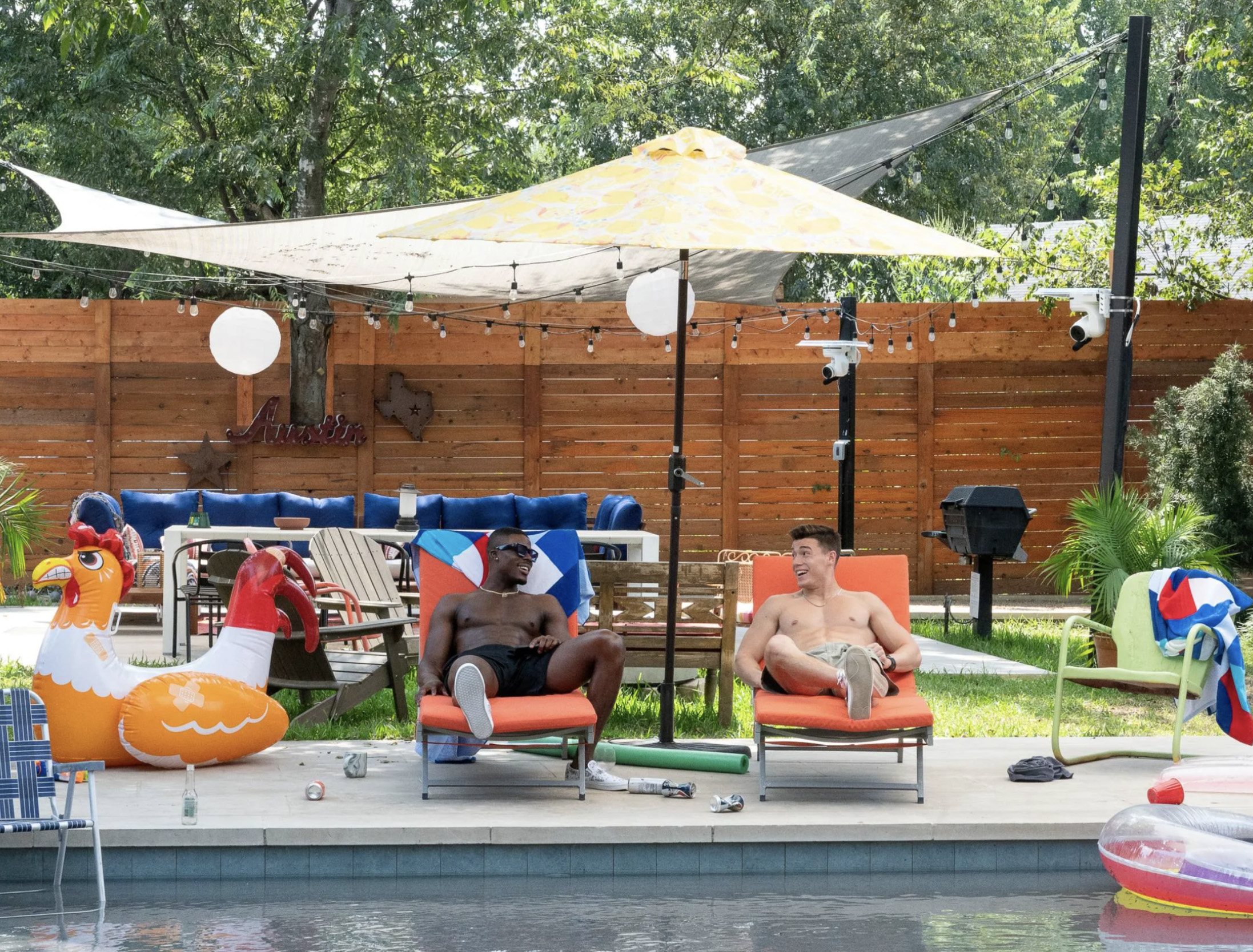 Two men sit on lounge chairs in front of a pool
