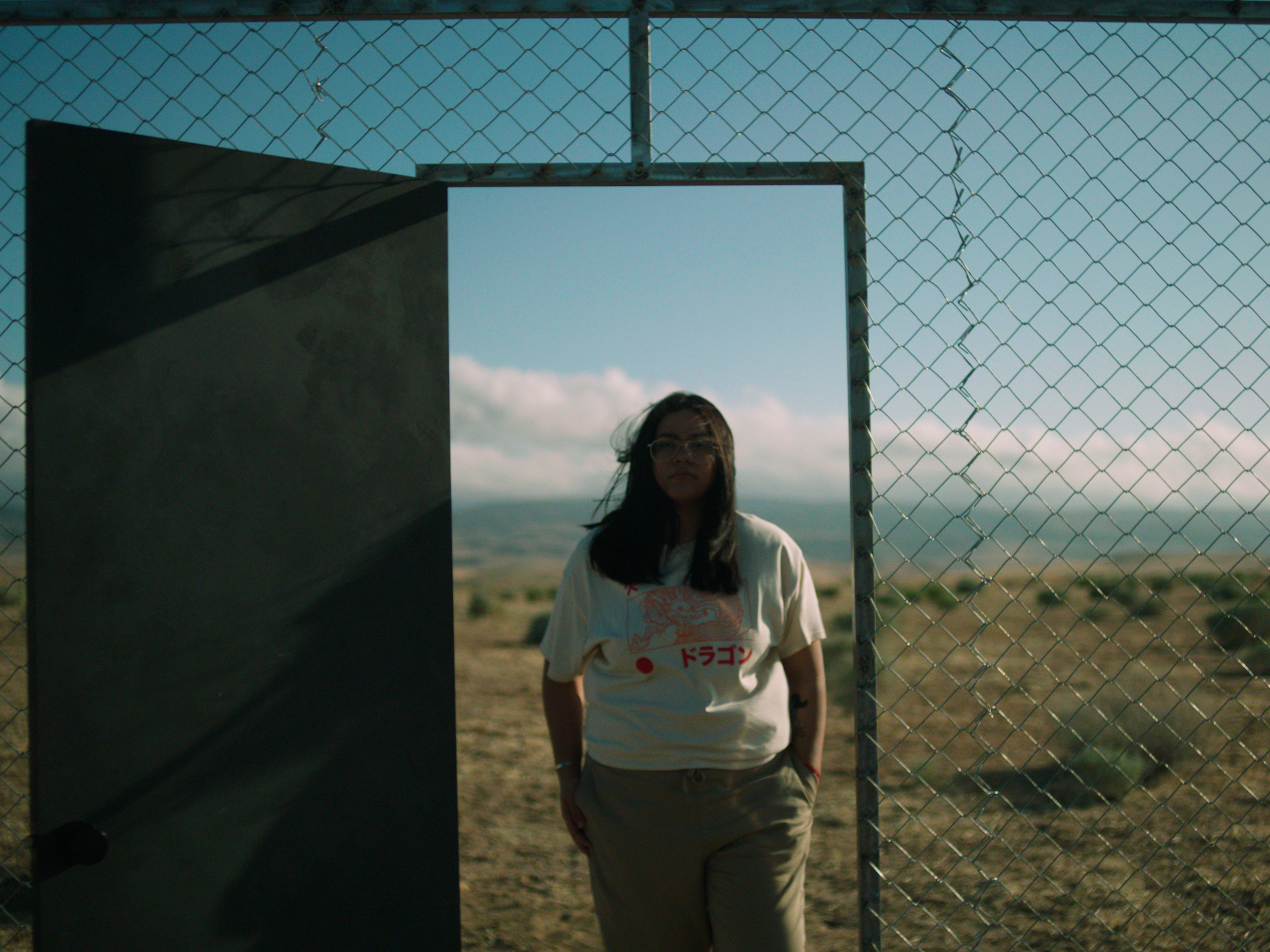 A woman is framed by a door opening that sits inside a chained fence