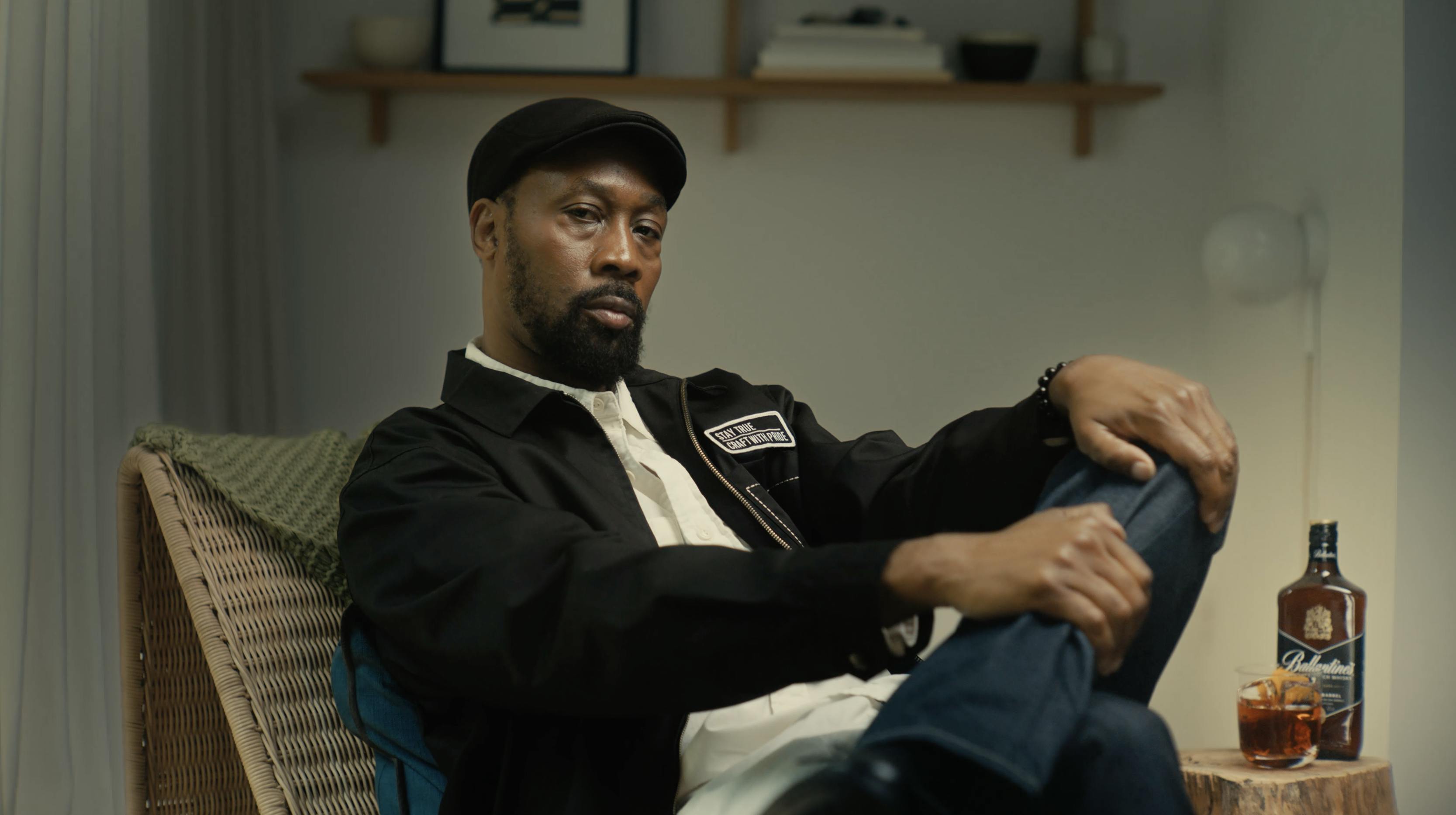 A man (RZA) sits next to a glass of Ballantine's whiskey