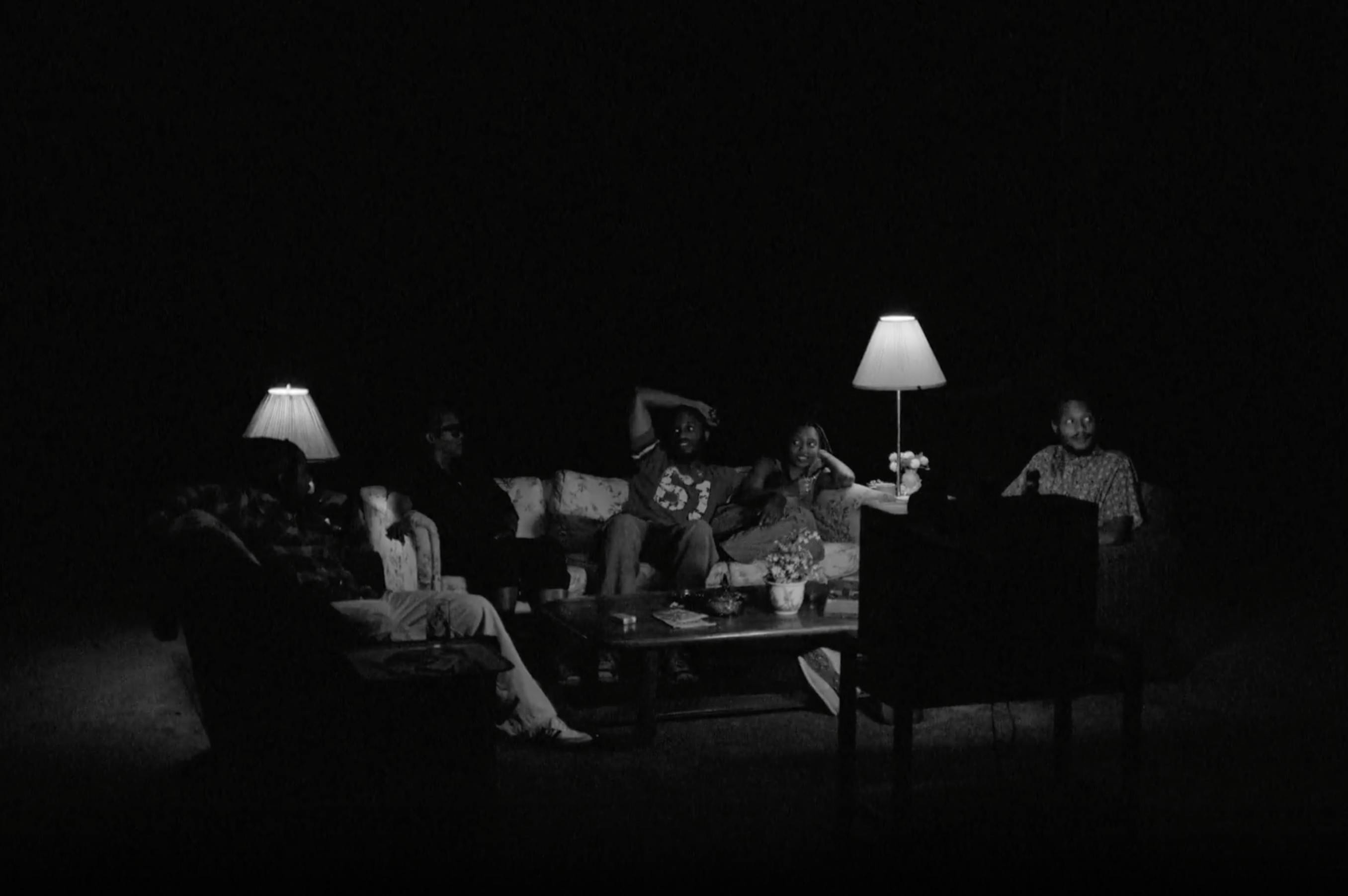 A black and white image of a group of people sitting in a dark room with two lamps glowing