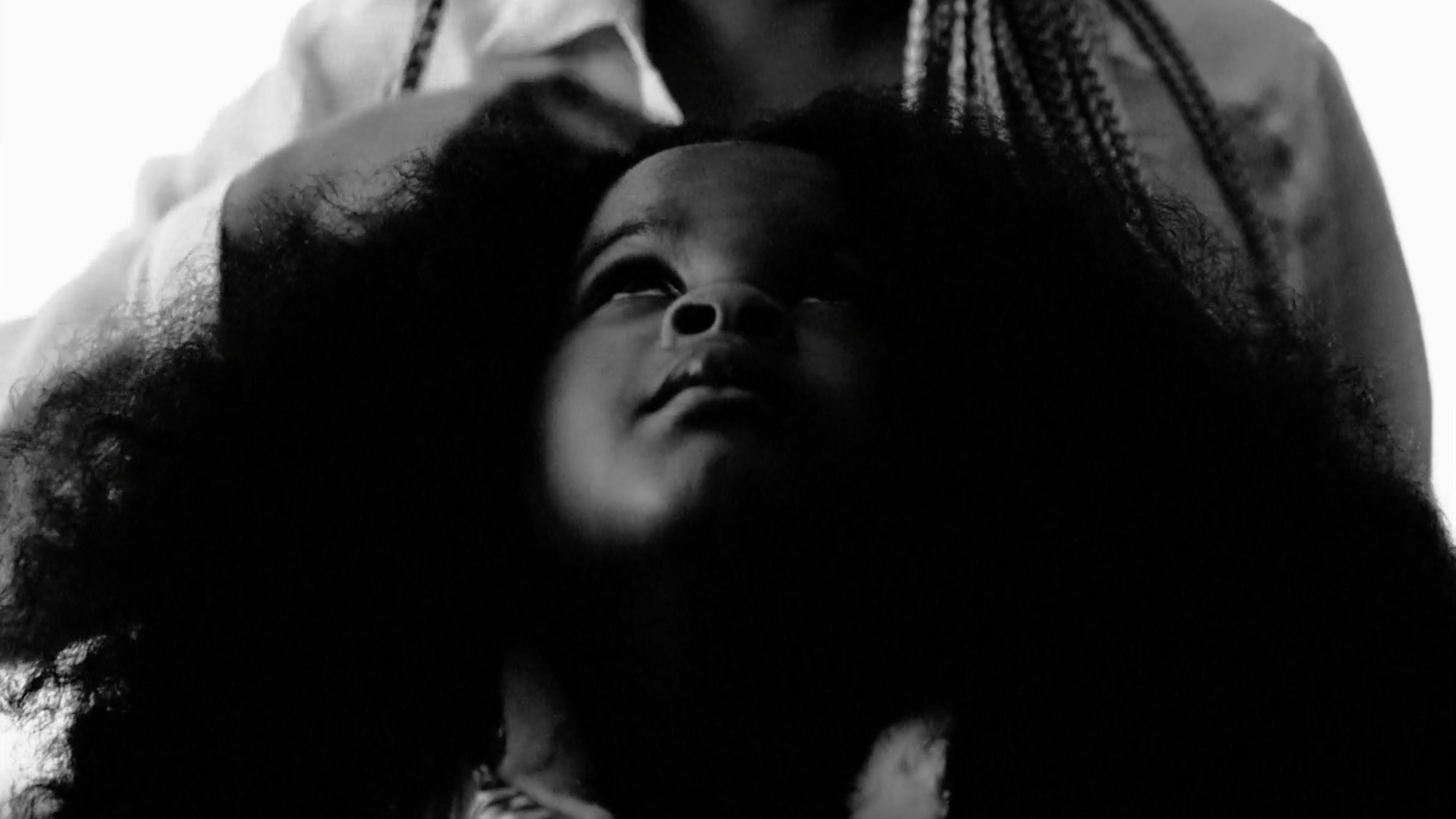 A black and white image of a child looking up while her hair is braided