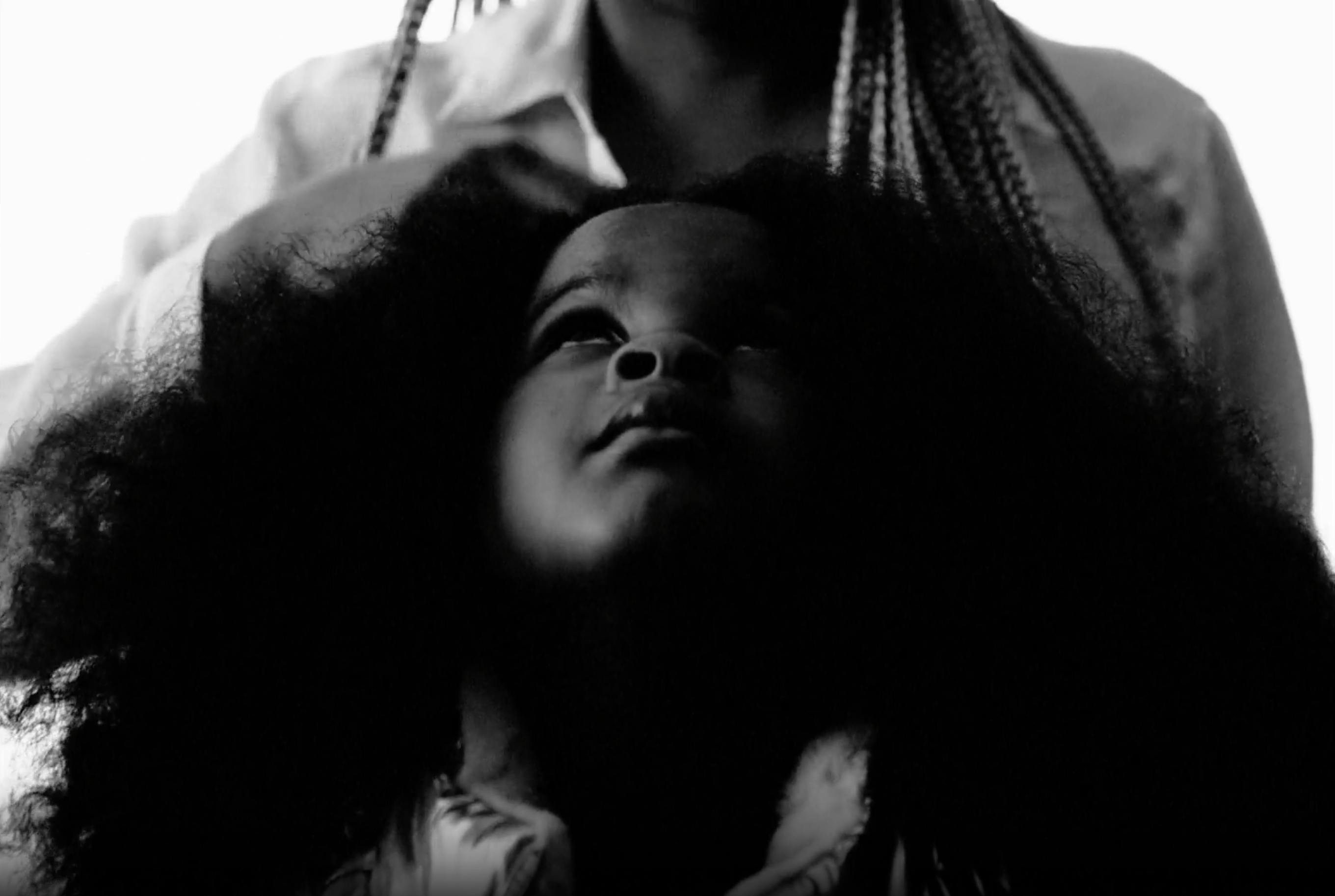 A black and white image of a child looking up while her hair is braided