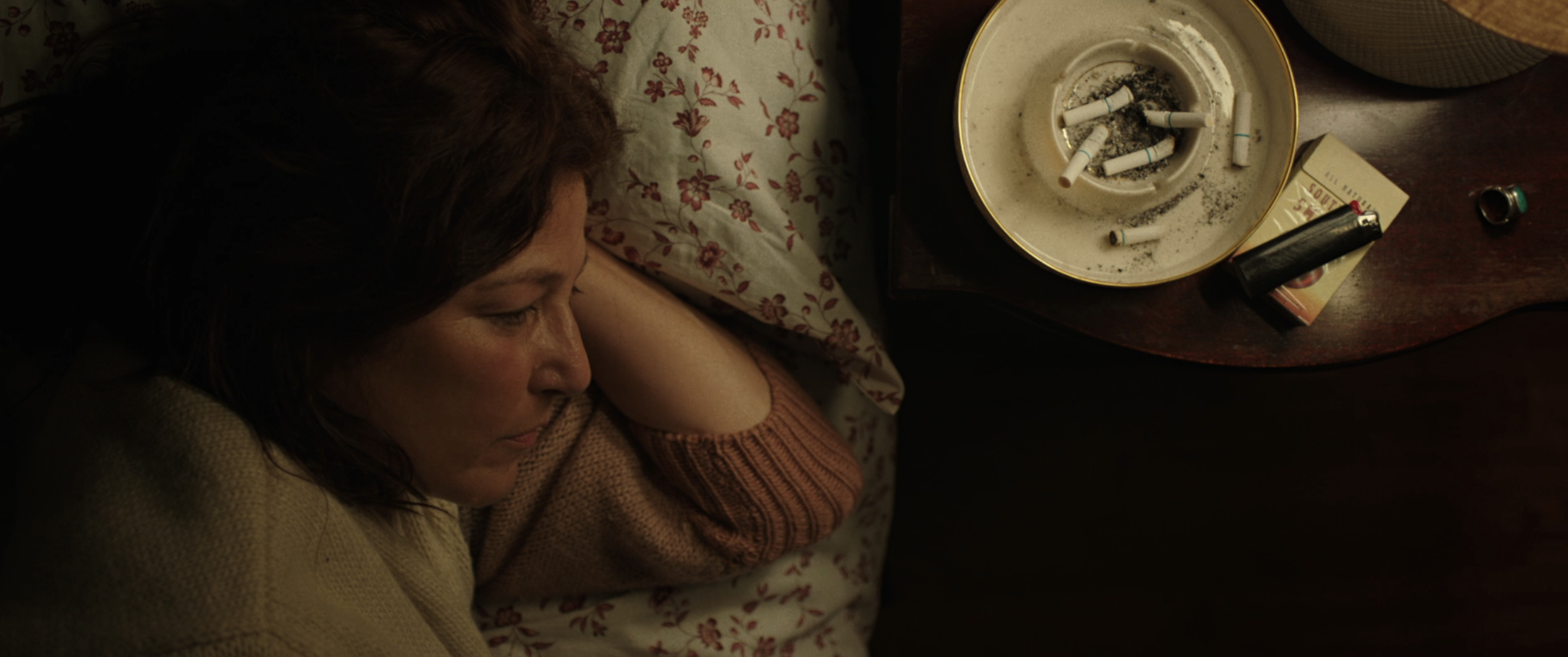 A woman lies in bed next to an ashtray with cigarettes