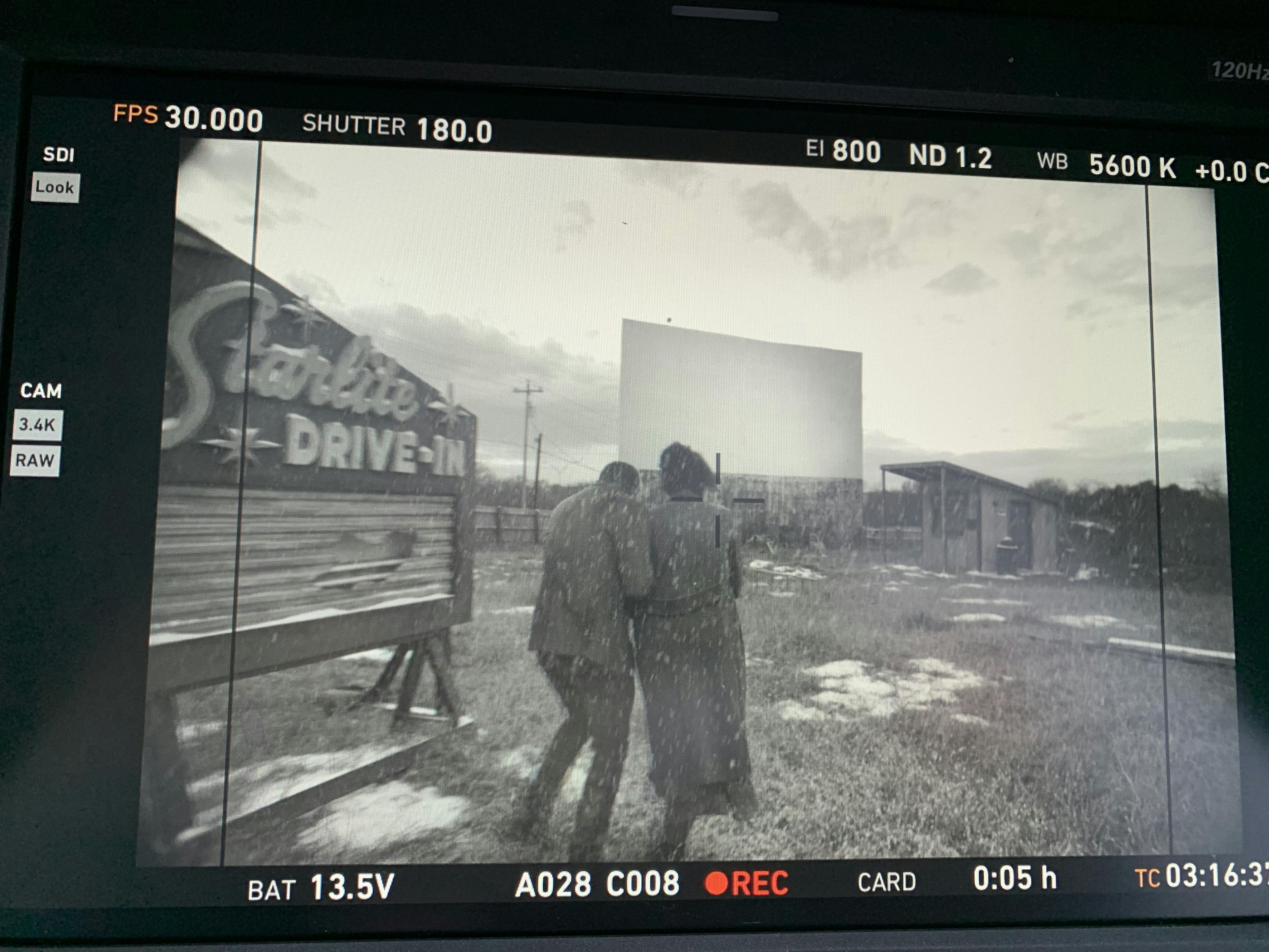 An image of a video camera screen showing two people walking into a drive-in movie theater