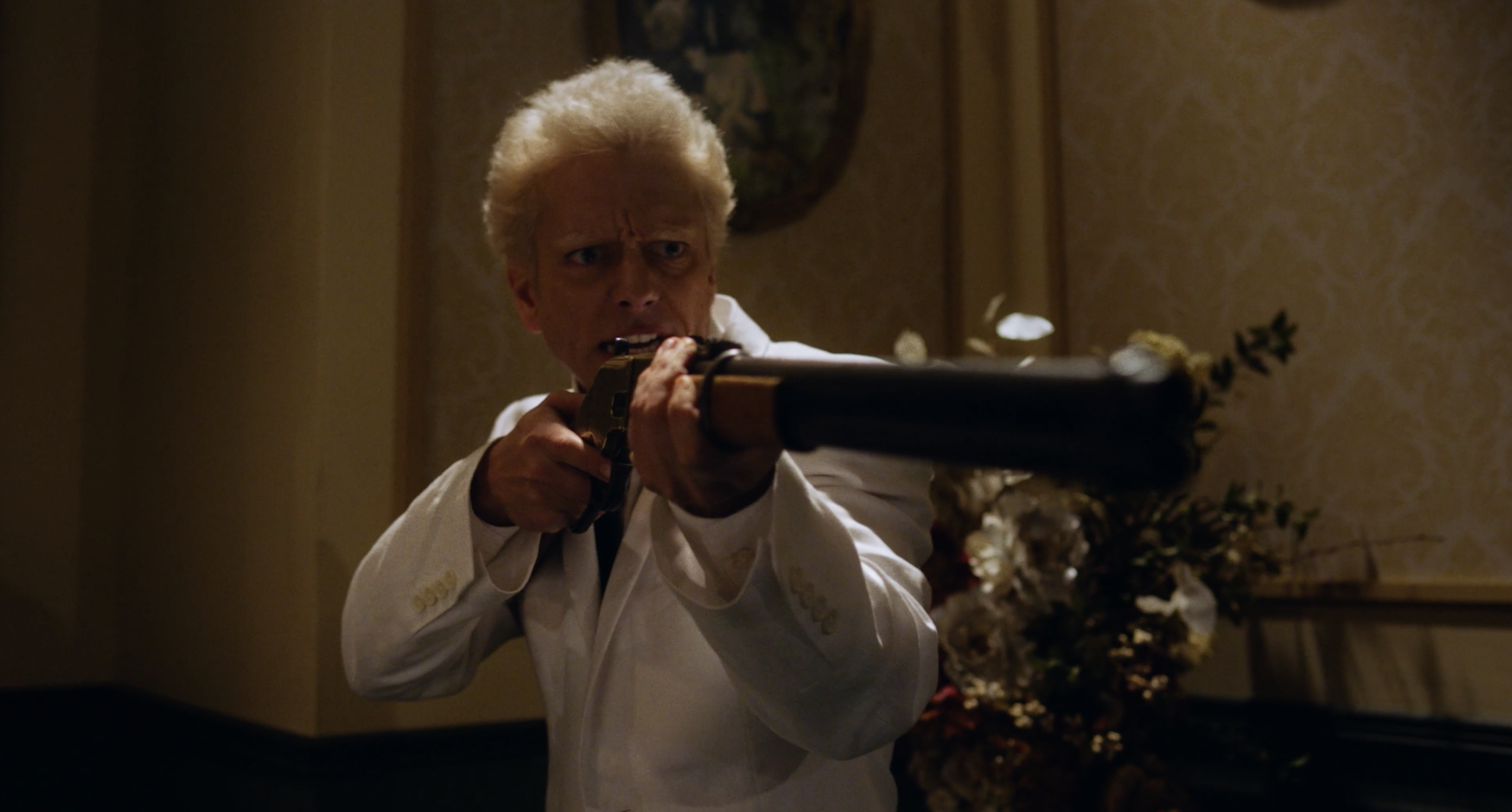A man in a white suit holds a shotgun