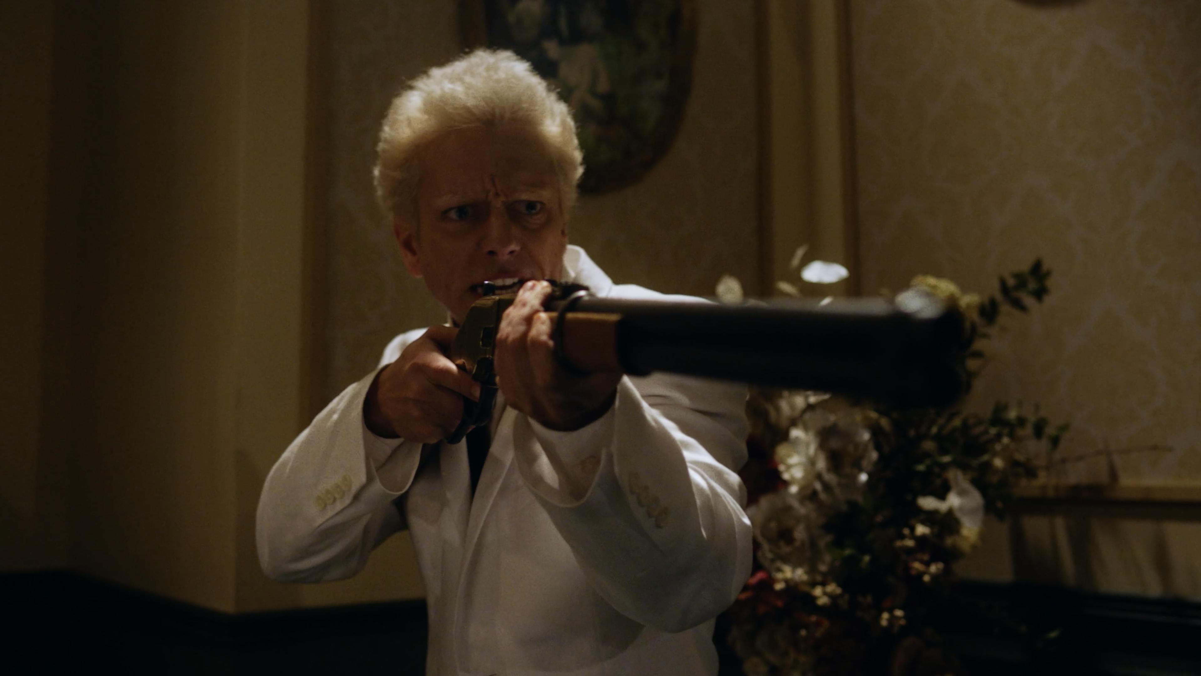 A man in a white suit holds a shotgun