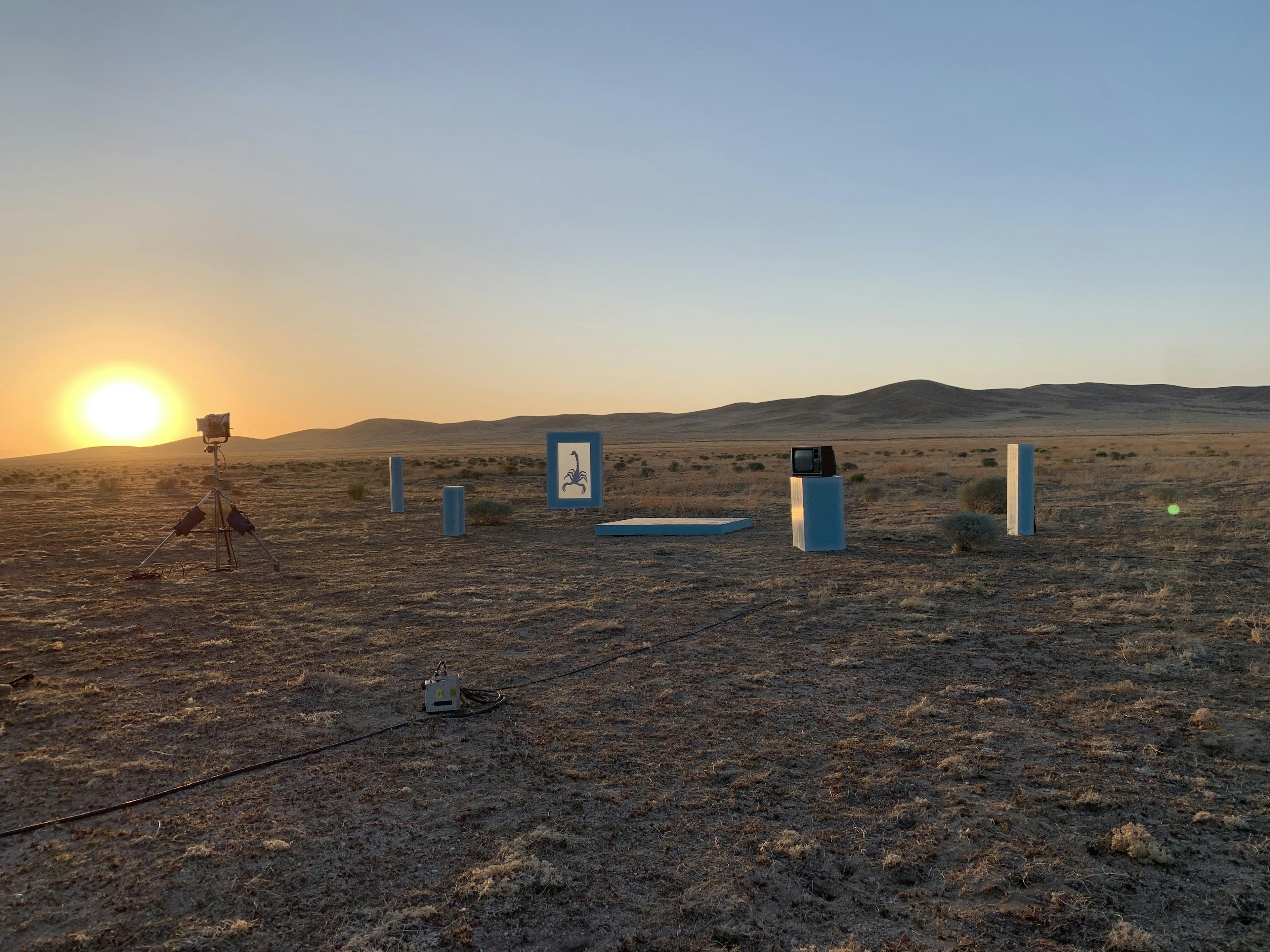 The sun sets over mountains in the horizon, with art exhibit frames structures in the foreground