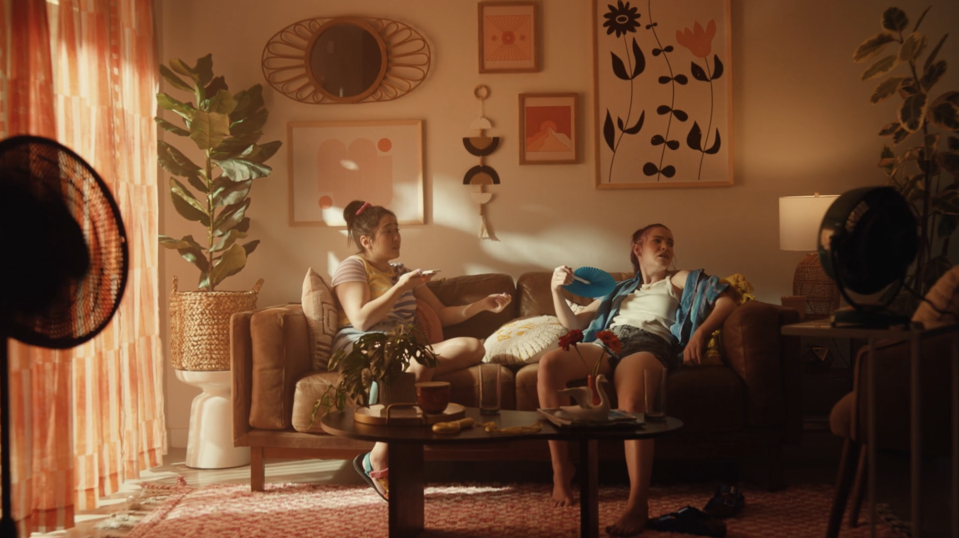 Two women sit on a couch in a sun-drenched room