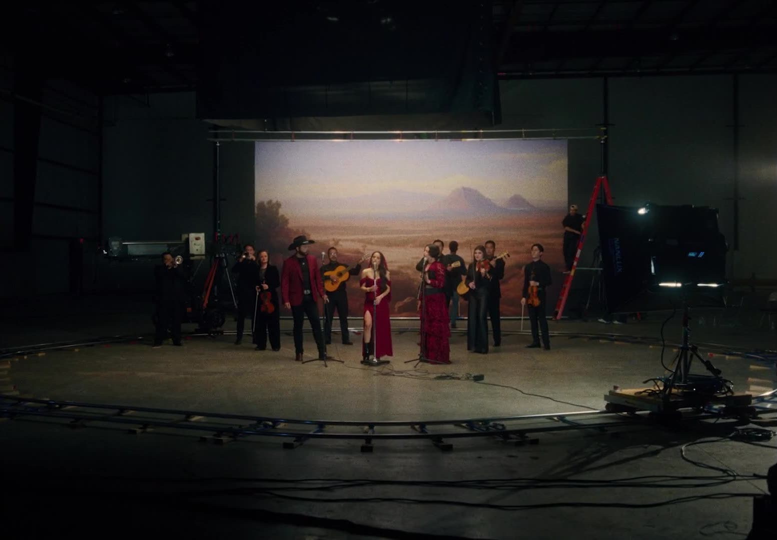 A group of three musicians in red and their ensemble in black stand in a studio