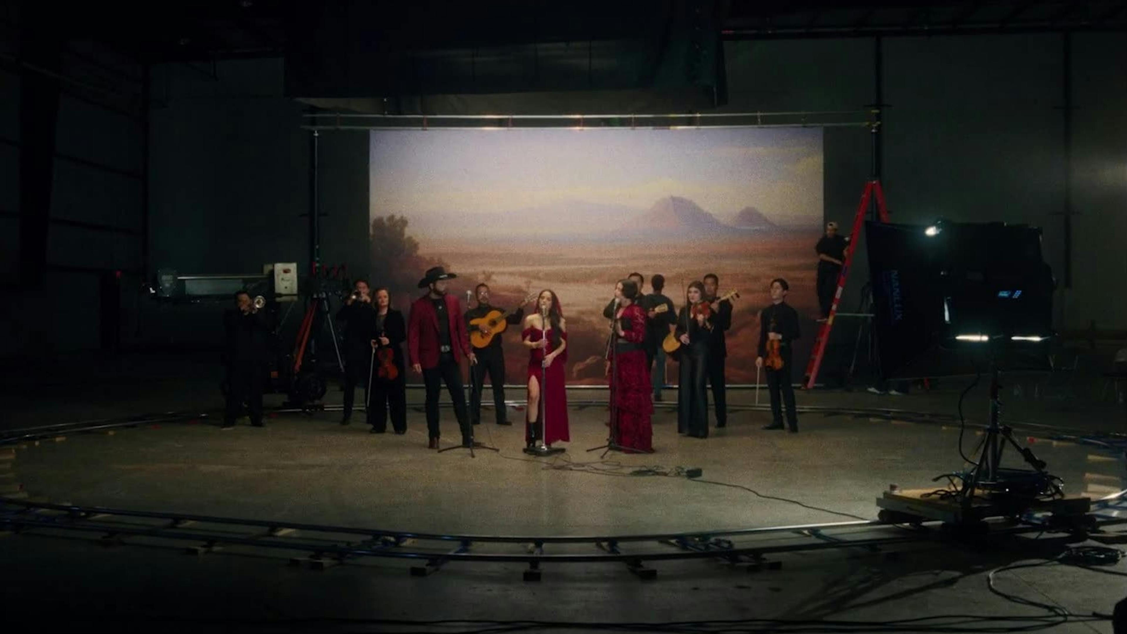 A group of three musicians in red and their ensemble in black stand in a studio