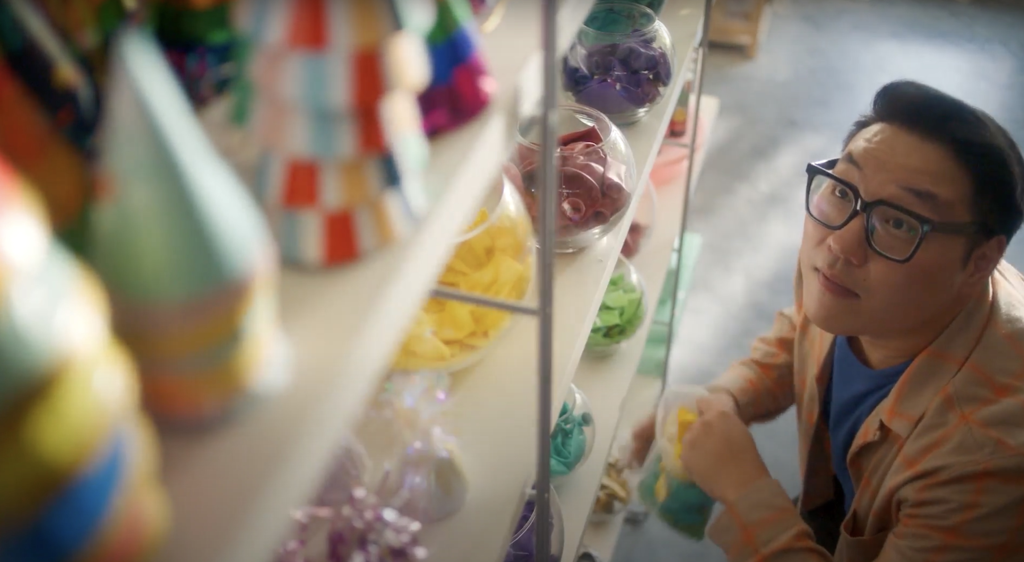 A man looks up at a shelf with colorful party supplies