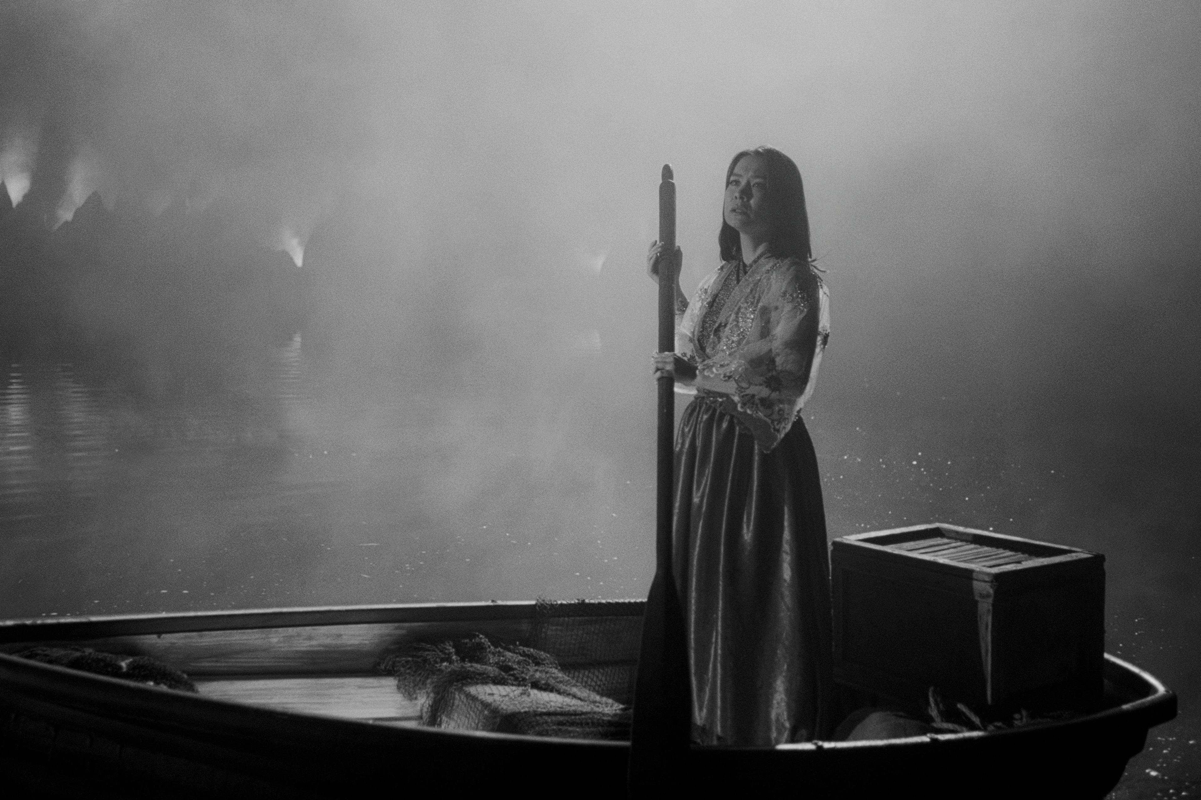 Mitski standing upright in the rowboat with an oar in her hand