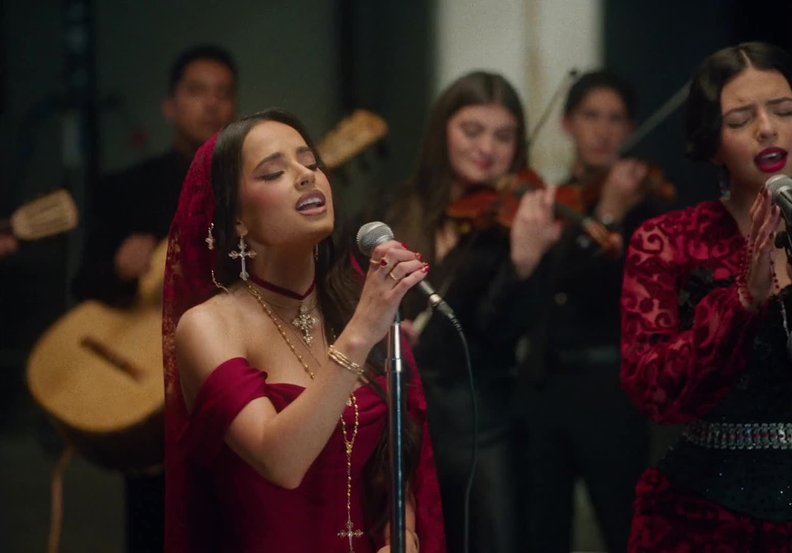 Two women in red sing into microphones with violins and a guitar in the background