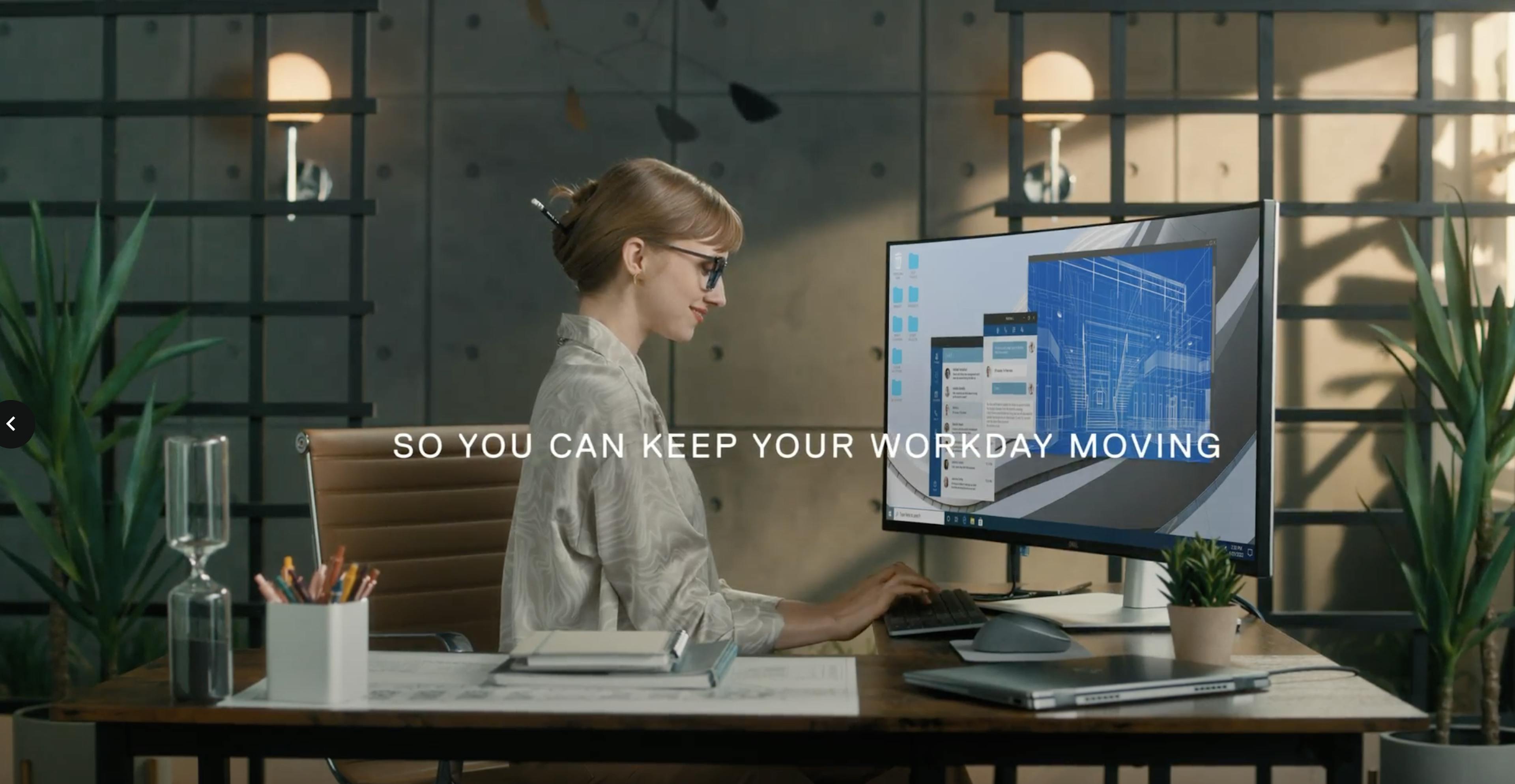 A woman sits in front of her large computer monitor with the text "So you can keep your workday moving"