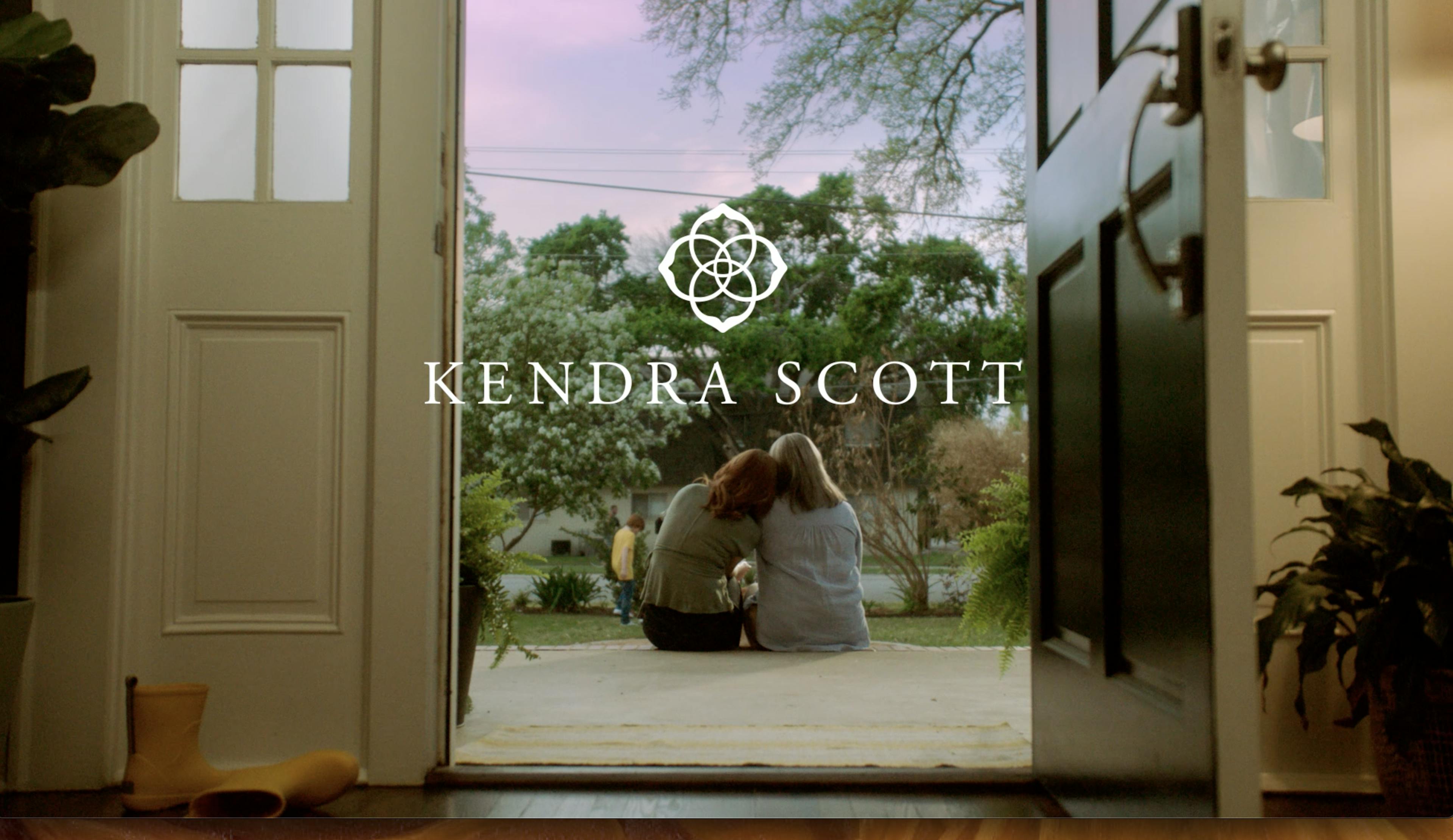 Viewed from the back, two women sit side by side on their front porch with the Kendra Scott logo overlaying the image