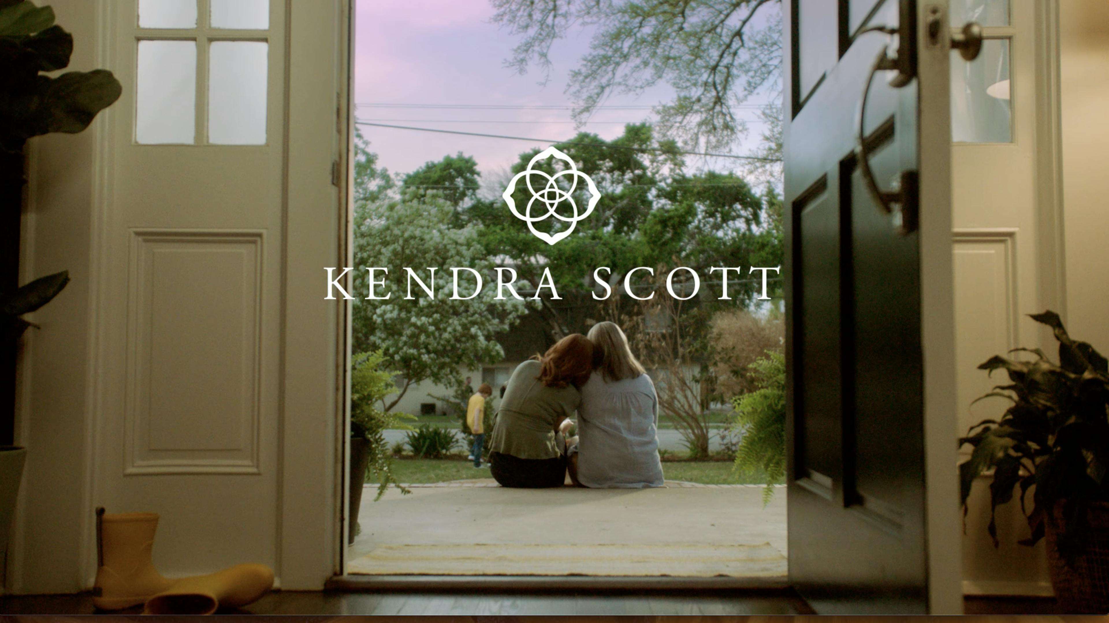 Viewed from the back, two women sit side by side on their front porch with the Kendra Scott logo overlaying the image