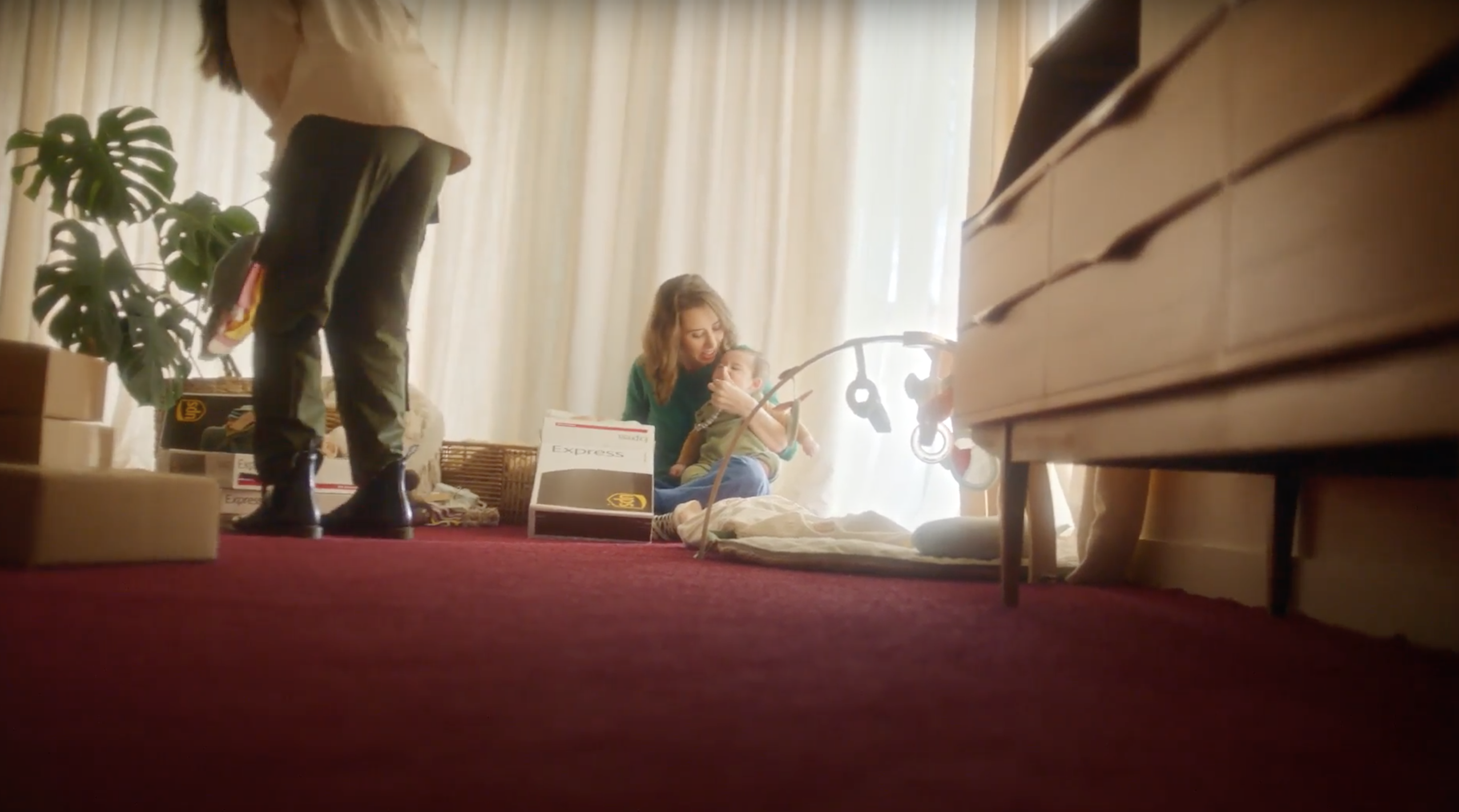 A woman holds a baby with next to an open UPS box with baby toys