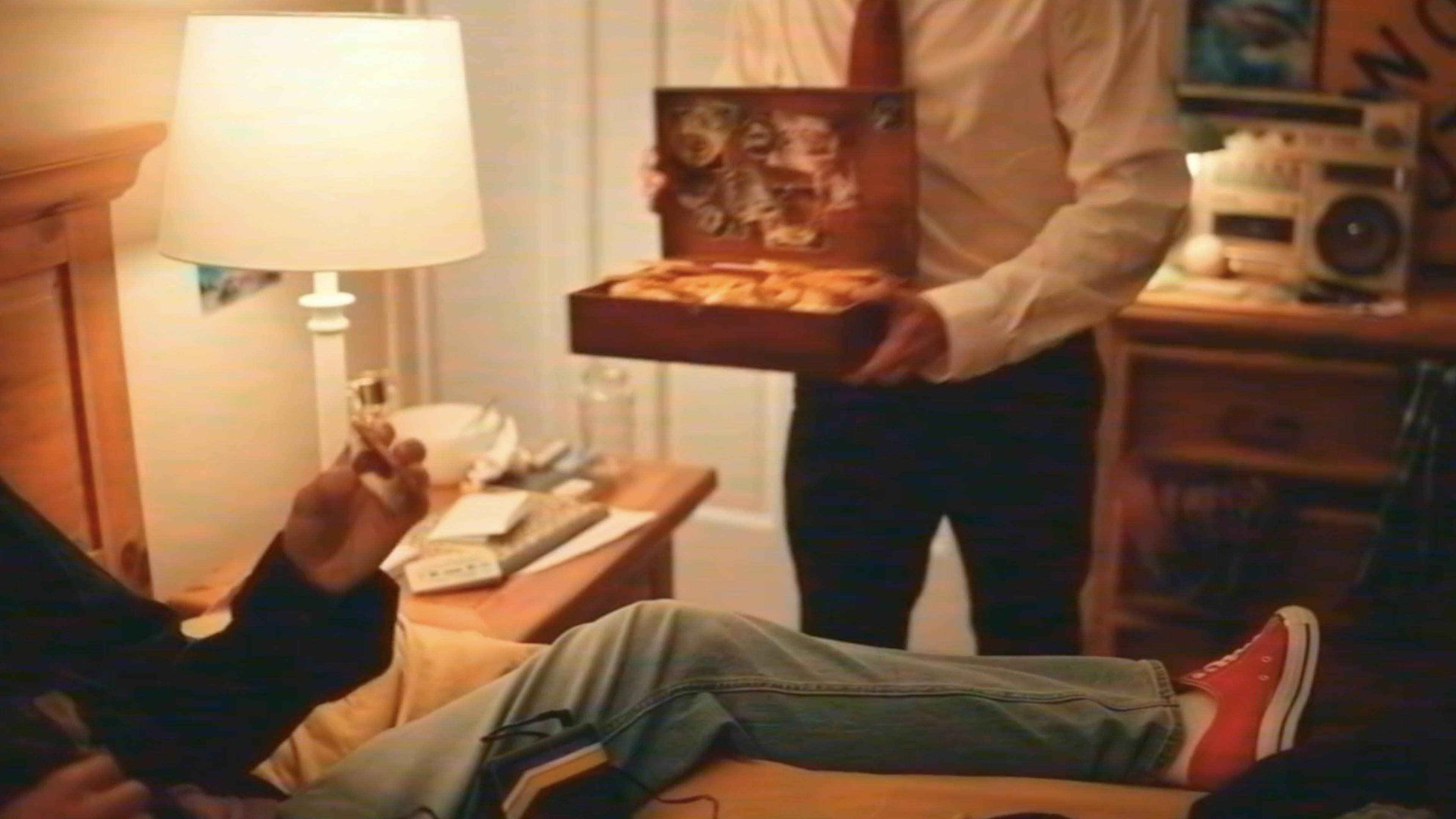 A man in a suit brings a box of food to someone laying in bed