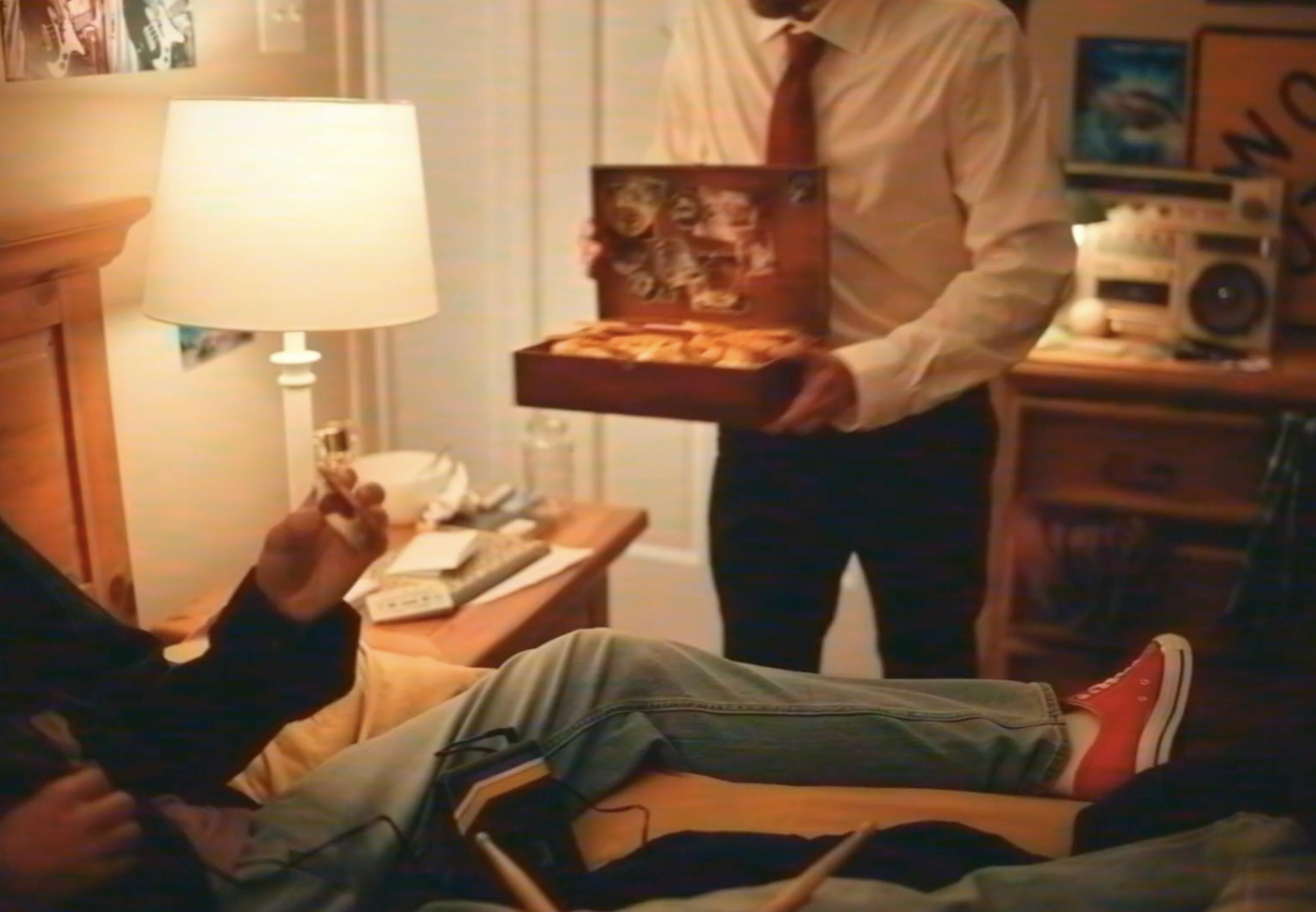 A man in a suit brings a box of food to someone laying in bed