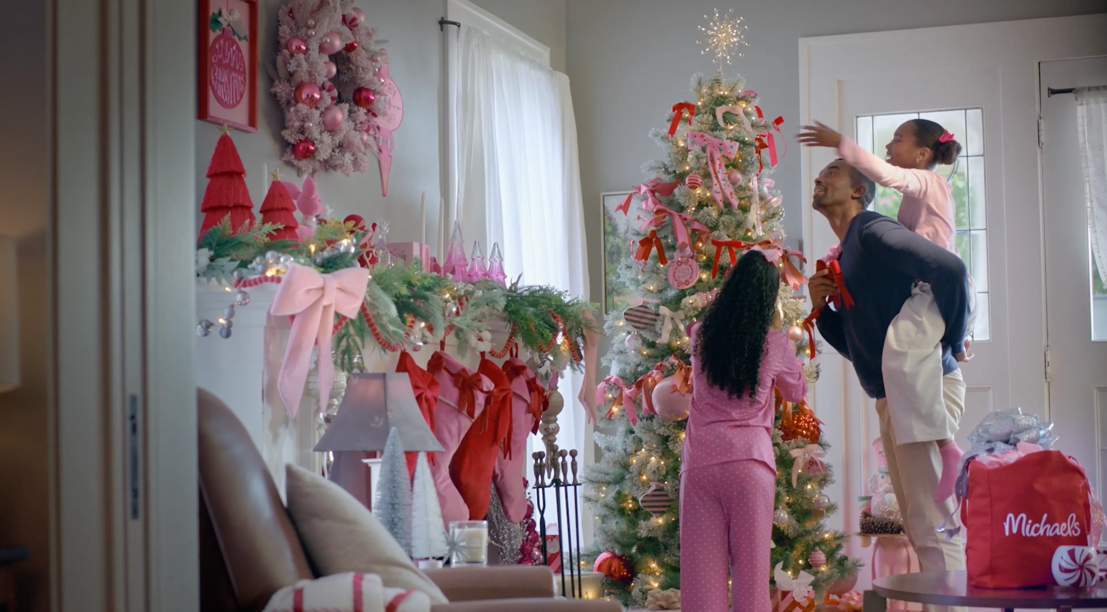 A father with 2 daughters decorating a pink christmas tree
