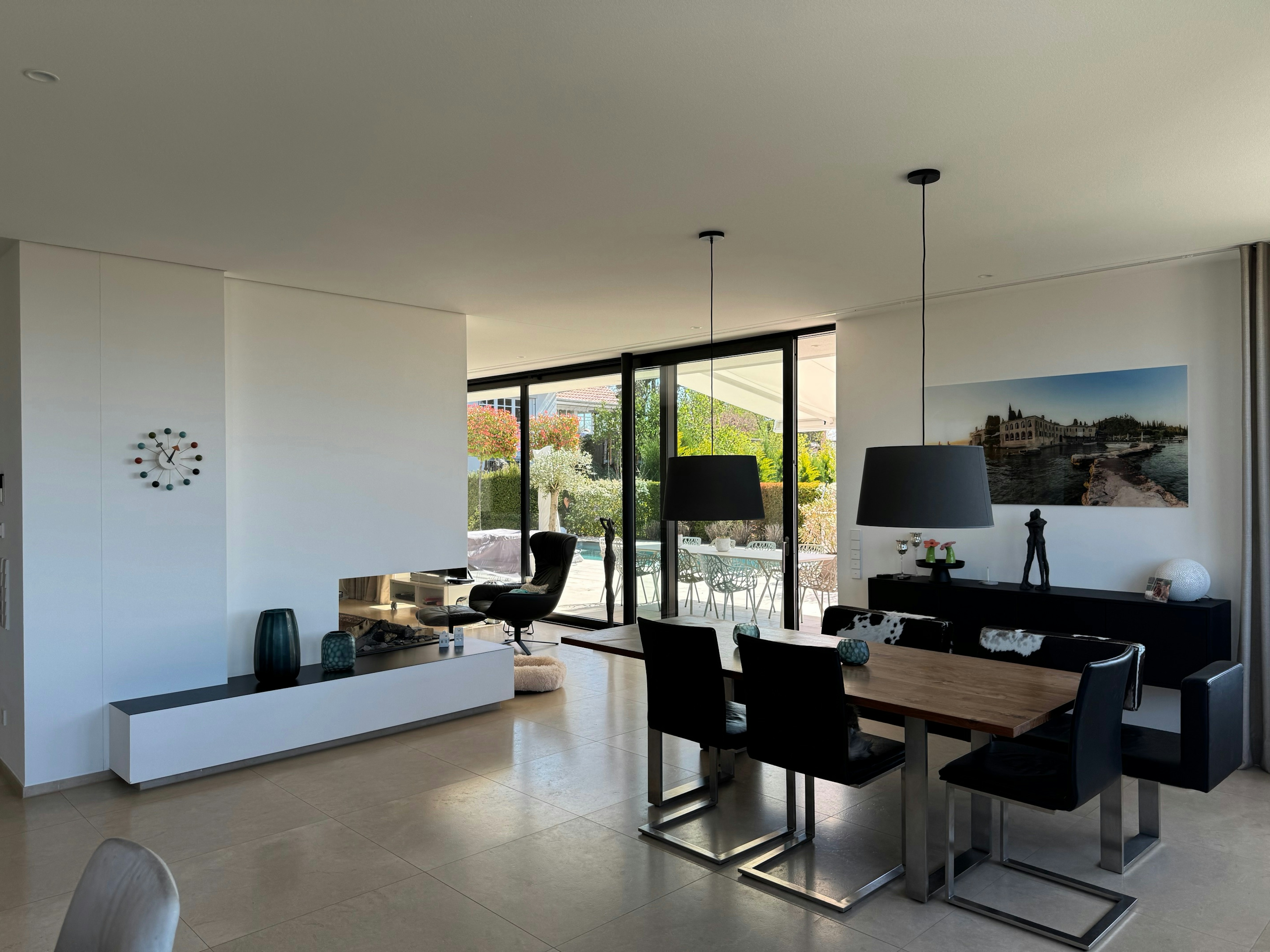 Offener Wohn-Essbereich mit direktem Zugang zur Terrasse und Poolanlage, bodentiefe Fenster und modernes Interieur mit Designleuchten.