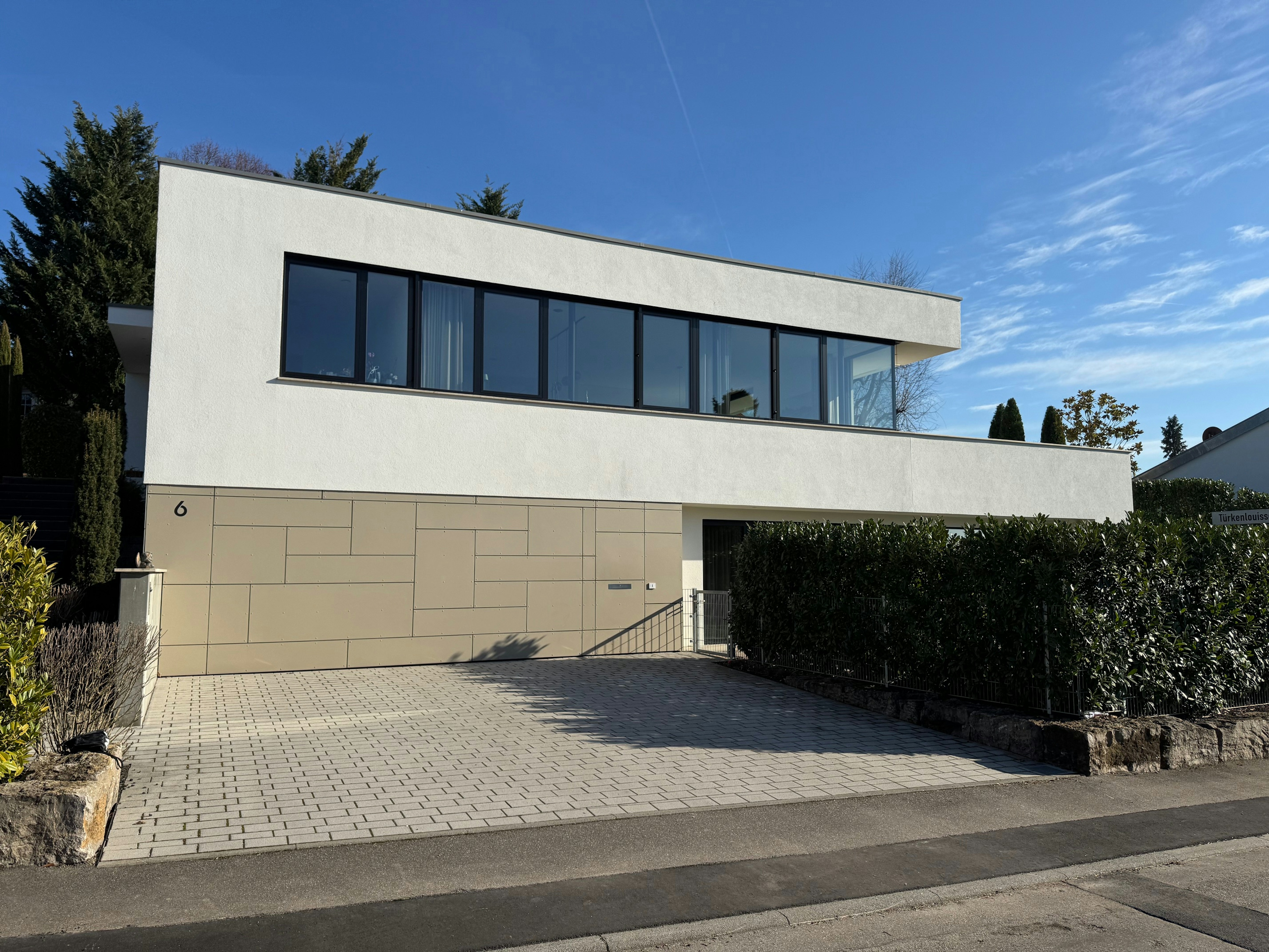 Moderne Straßenansicht des weißen Einfamilienhauses mit Flachdach und großer Fensterfront, realisiert vom Architekturbüro Bauer im Jahr 2018.