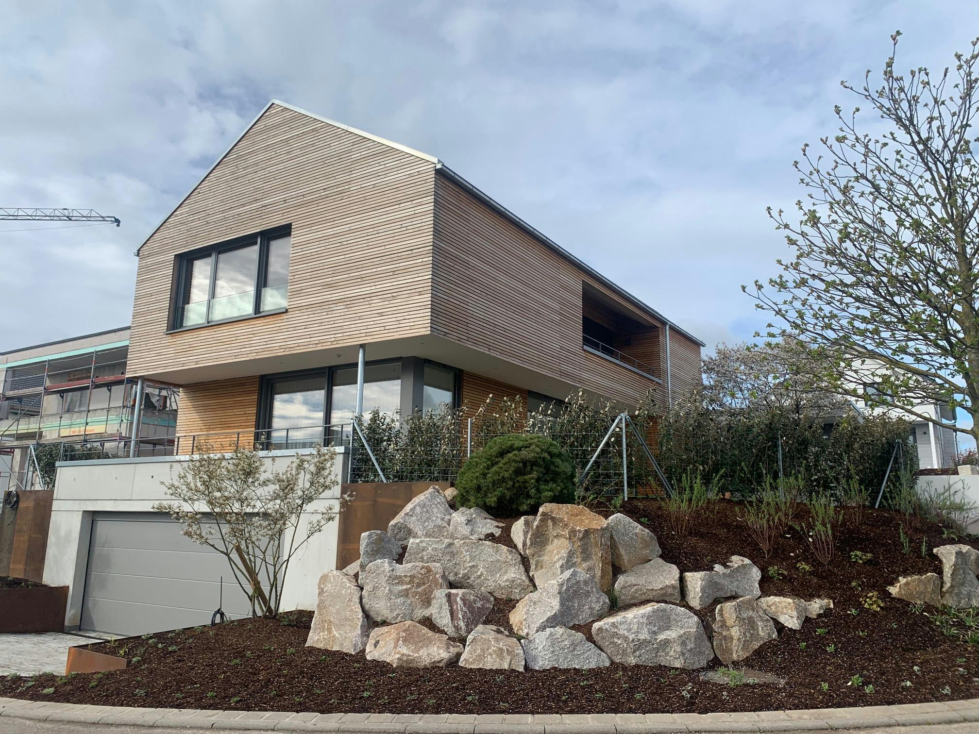 Moderne Straßenansicht eines Wohnhauses mit Holzfassade und Betongarage – realisiert vom Architekturbüro Bauer im Jahr 2022.