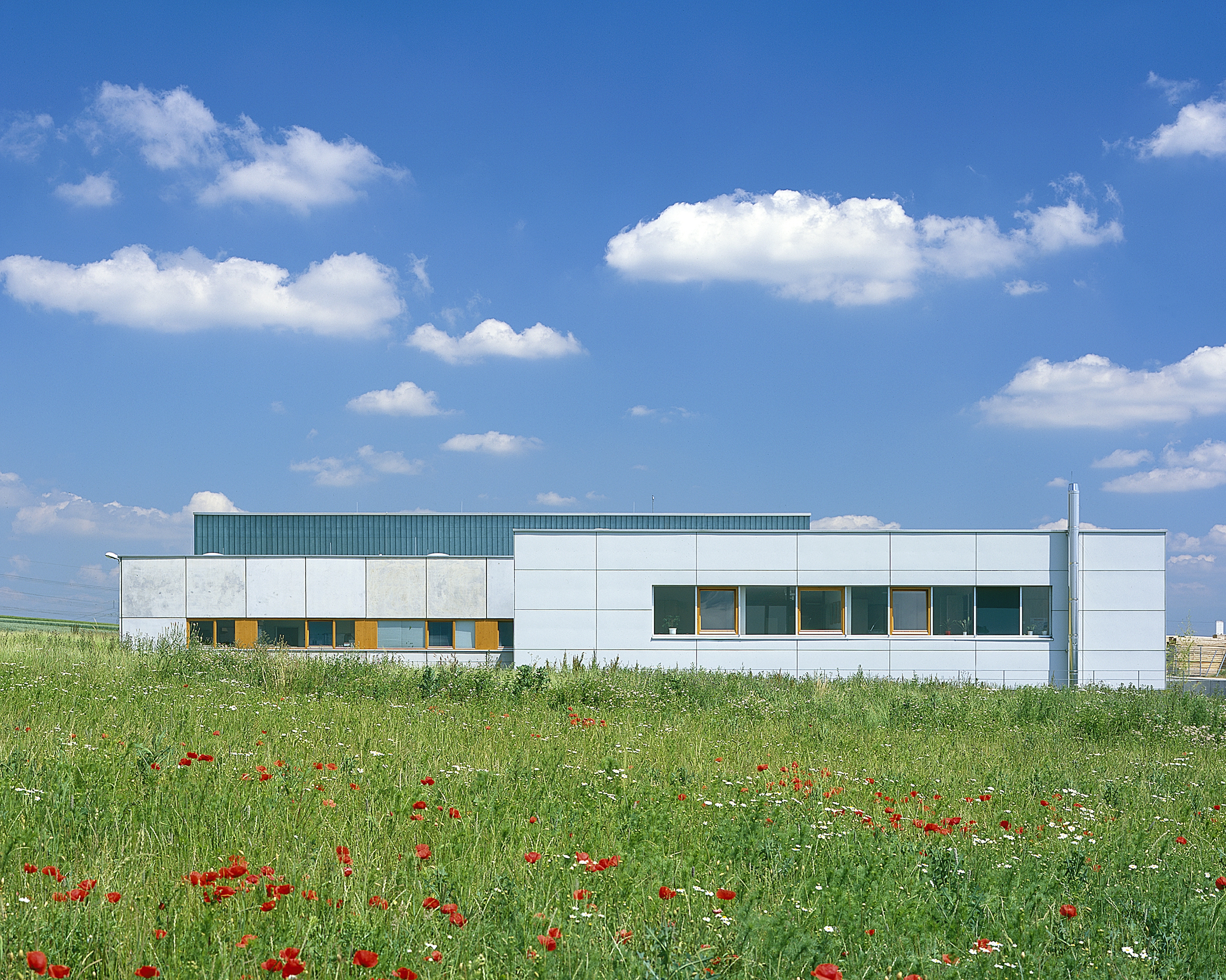 Frontansicht des Büro- und Lagergebäudes „Layer-Chemie“ mit klarer Fassadengliederung, begrüntem Vorbereich und modernem Flachdachdesign.